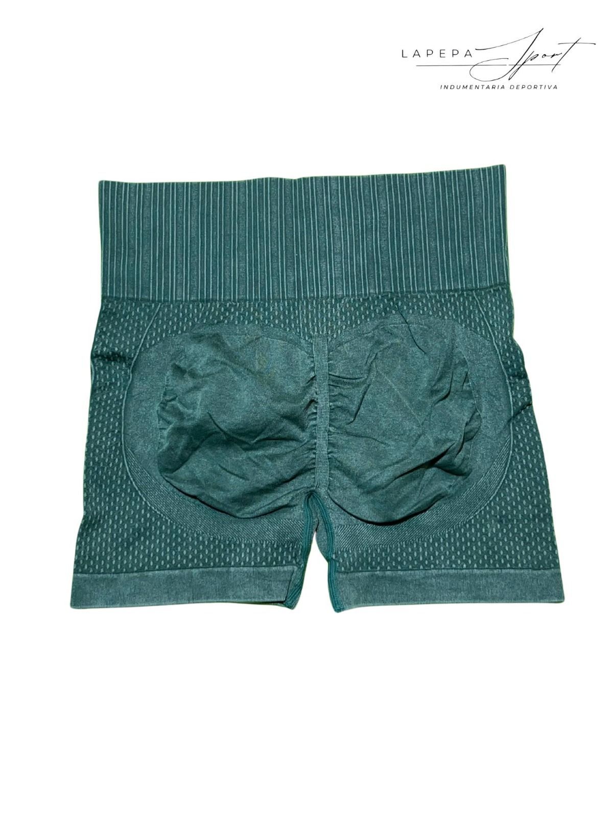 Mujer con top blanco y pantalones cortos verdes texturizados, de pie de espaldas al espectador.