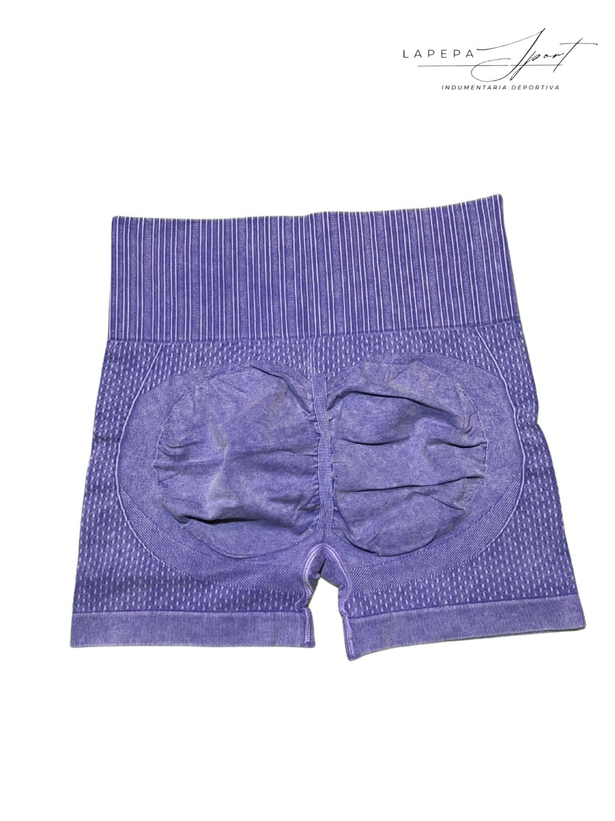 Mujer con pantalones cortos color lavanda, de espaldas, sonriendo, en un estudio.