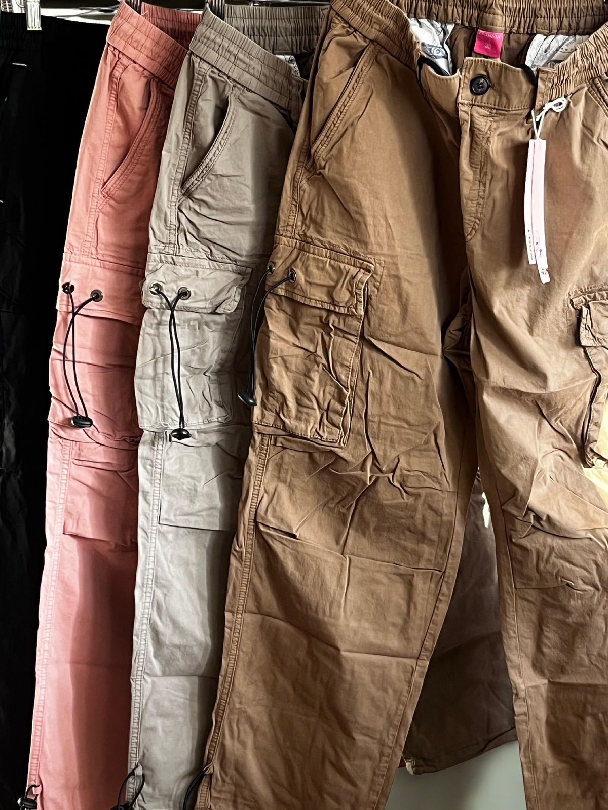 Mujer con camiseta negra y pantalones cargo marrones, sonriendo, con gafas y zapatillas blancas.