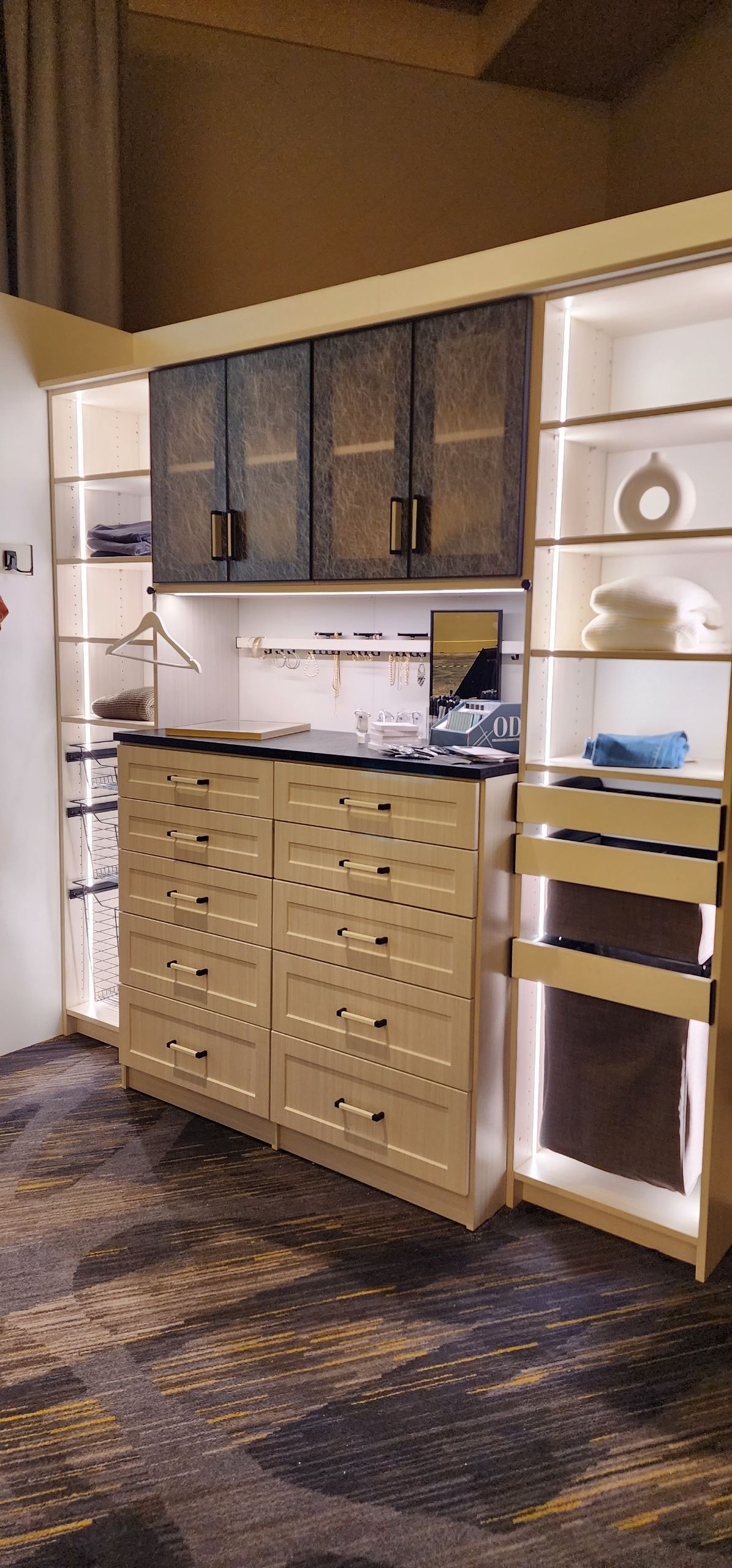 A modern custom closet system with lighted shelves, wooden drawers, and patterned cabinet doors in a bedroom setting.