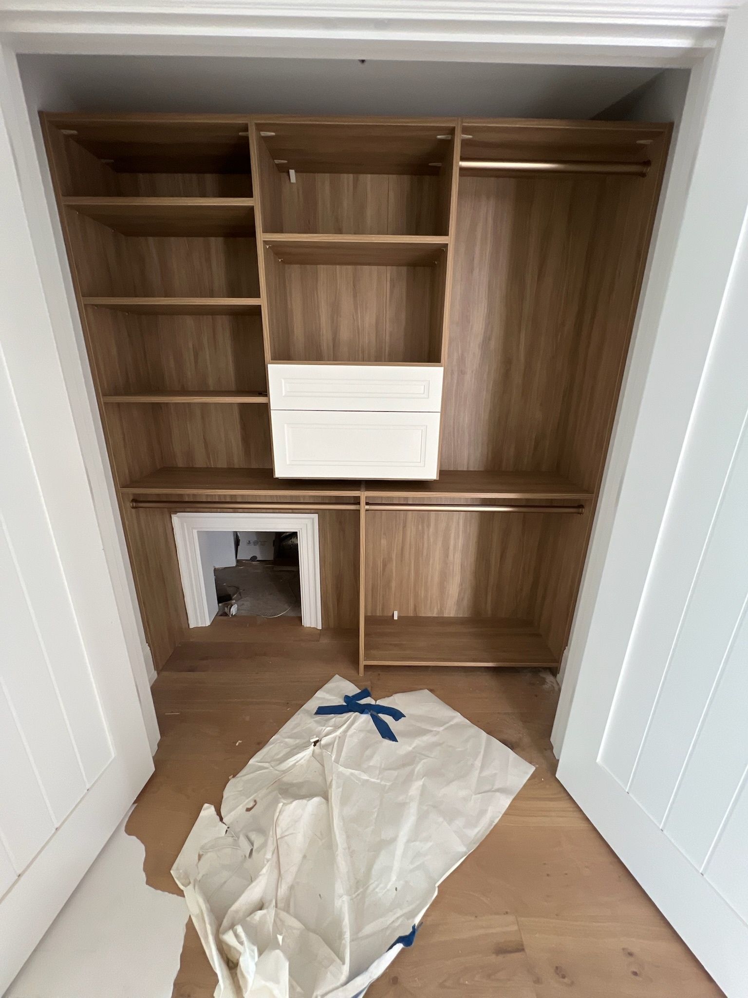 A wooden wardrobe installation inside a closet, featuring shelves, two white drawers, and a lower cubby opening.