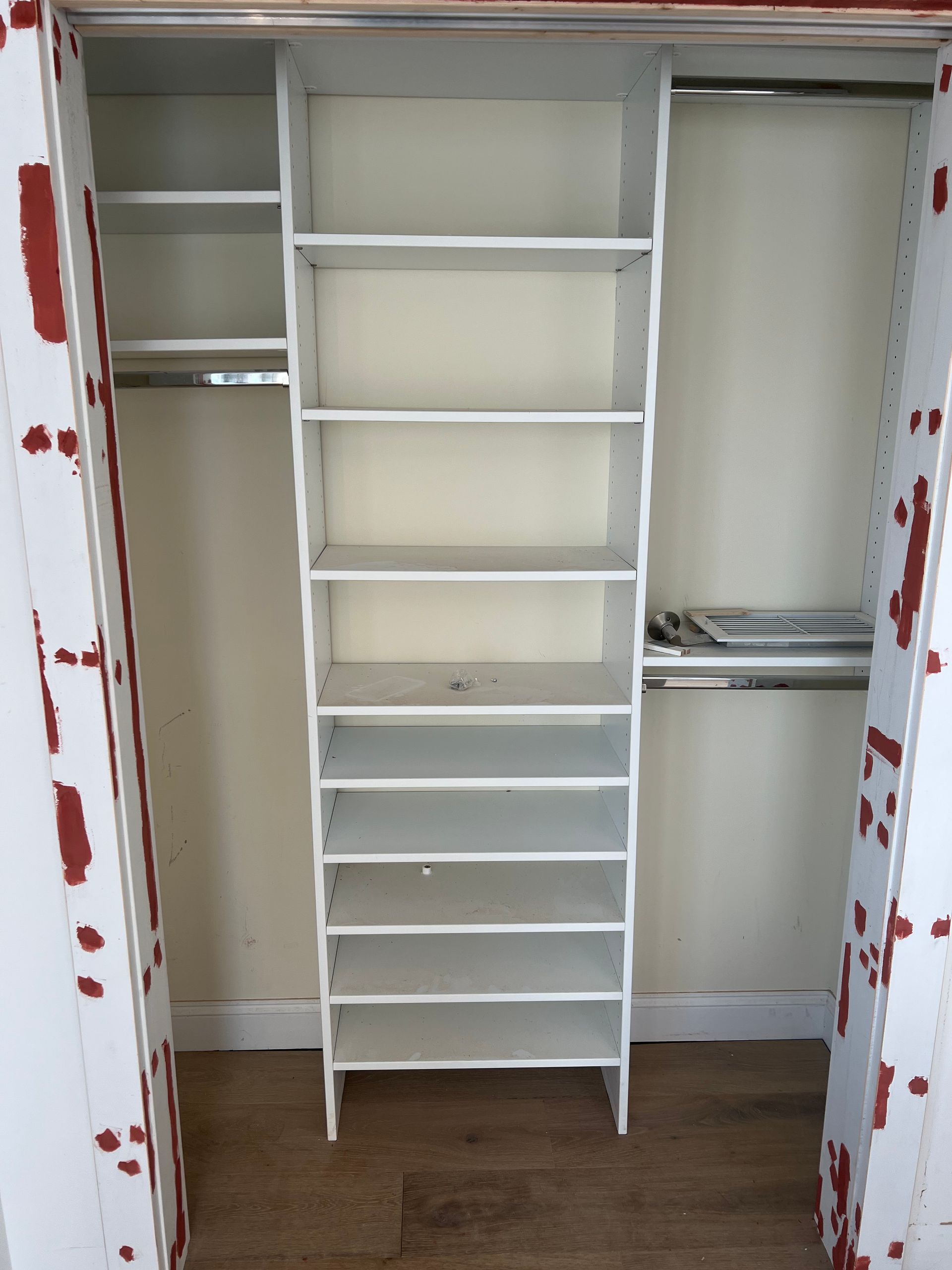 A white closet organizer unit with multiple shelves sits between two hanging rods; the surrounding door frame is peeling.
