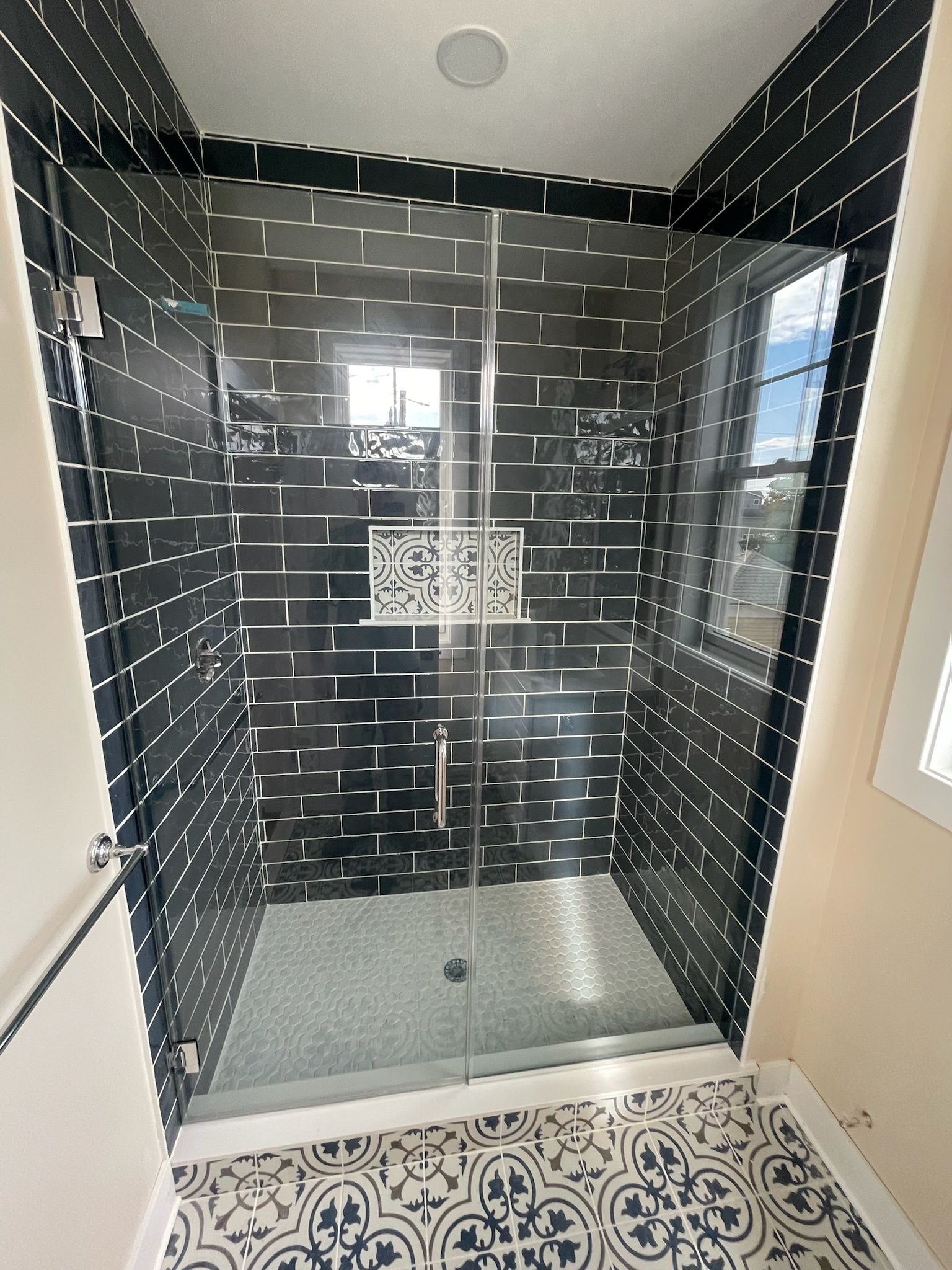 A glass shower stall with black-and-white subway tile walls and a decorative patterned tile niche, on a tiled floor.