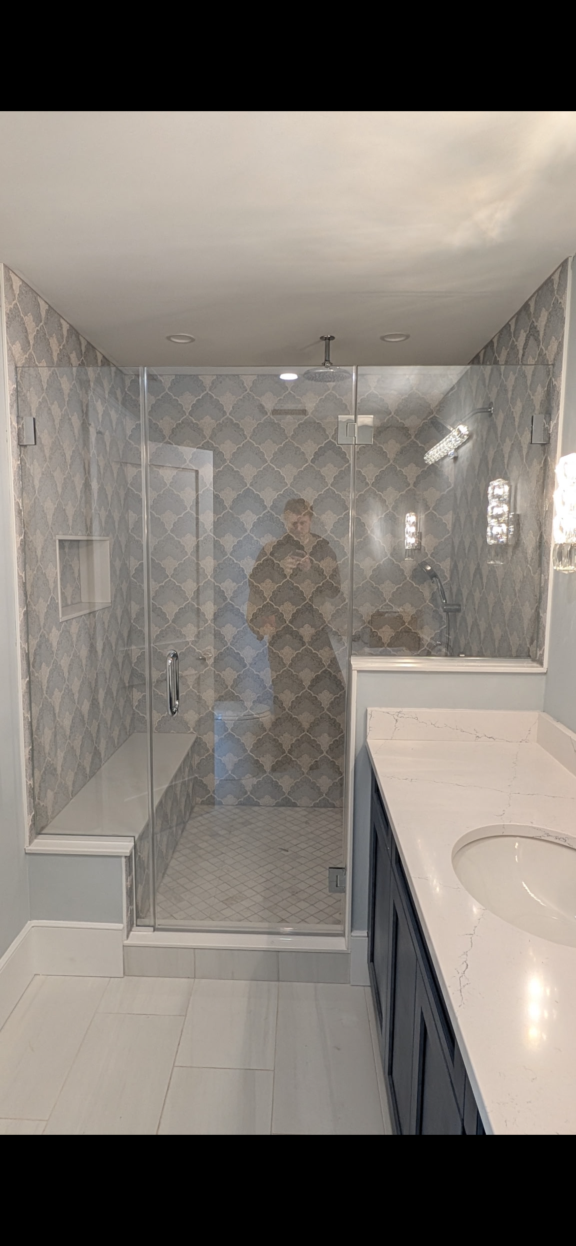 A modern bathroom featuring a walk-in glass shower with patterned tile, a built-in bench, and a white vanity countertop.
