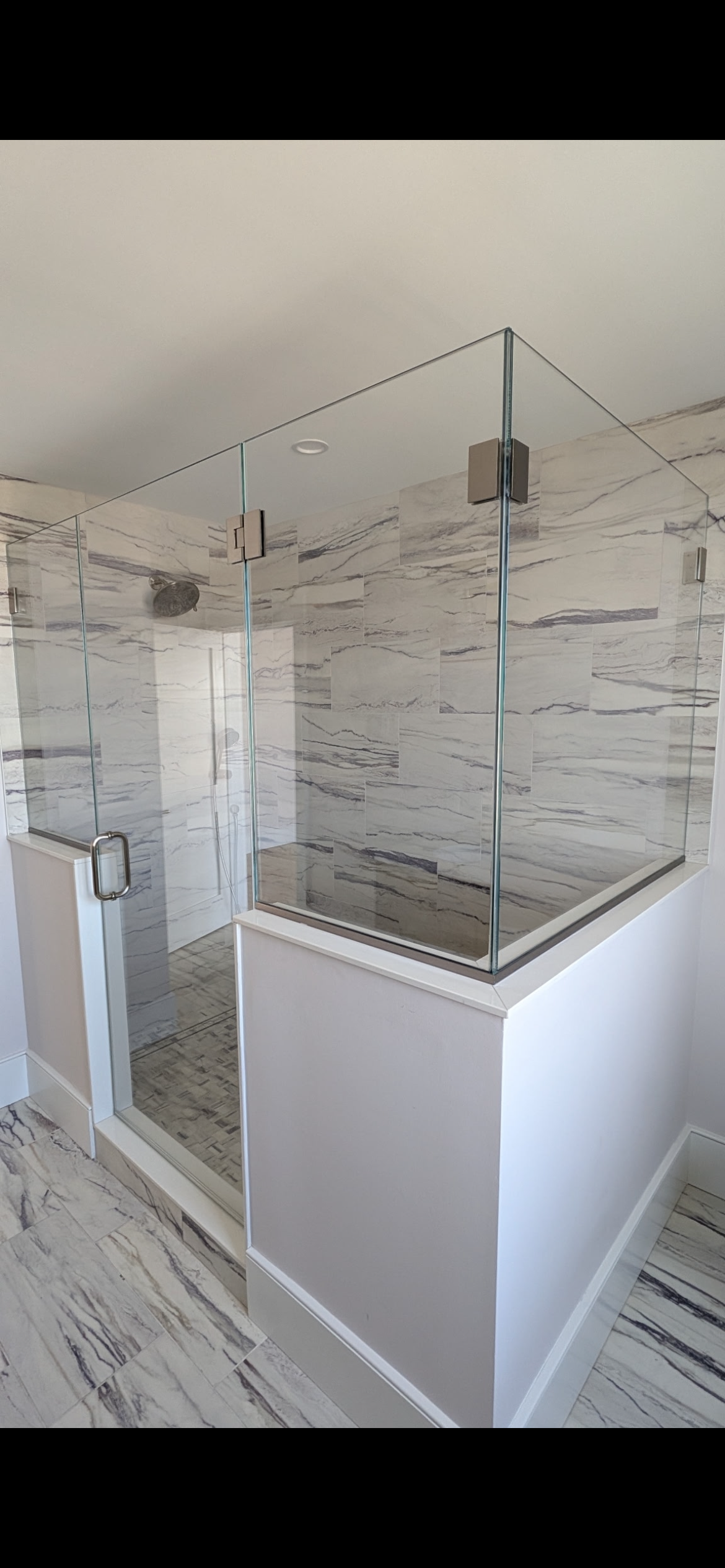 Modern glass shower enclosure with marble-patterned tile walls and floor in a bright, contemporary bathroom.