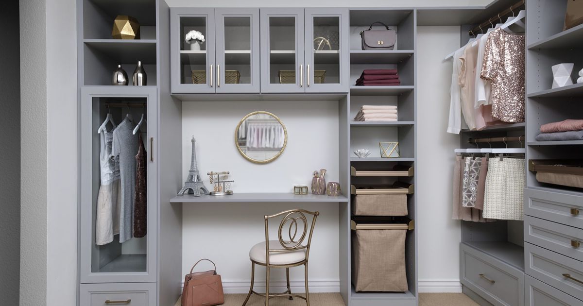 Gray walk-in closet with desk, chair, clothes, shelves, storage bins, and accessories.