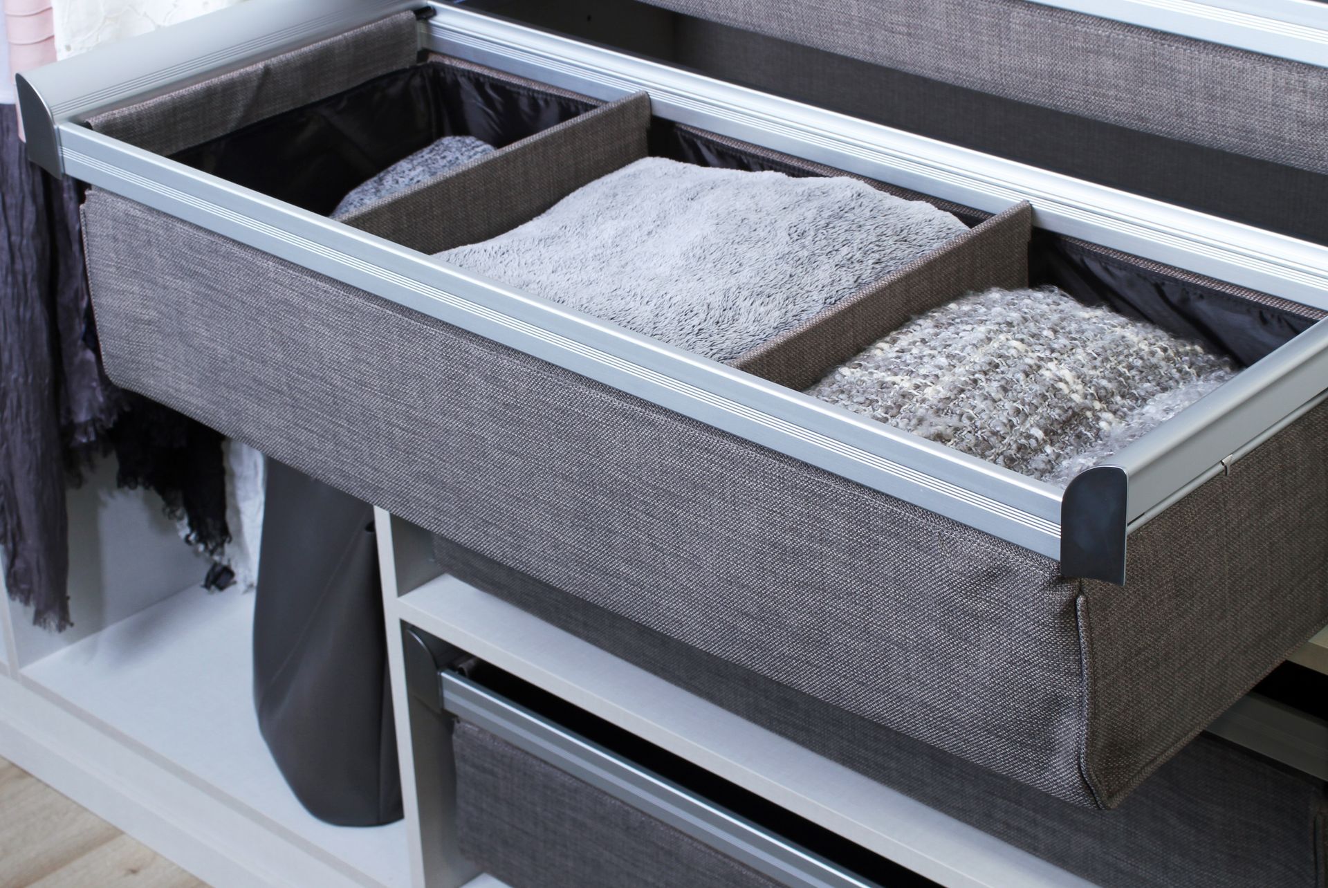 An open, grey fabric-lined closet drawer featuring two dividers and organized folded items.