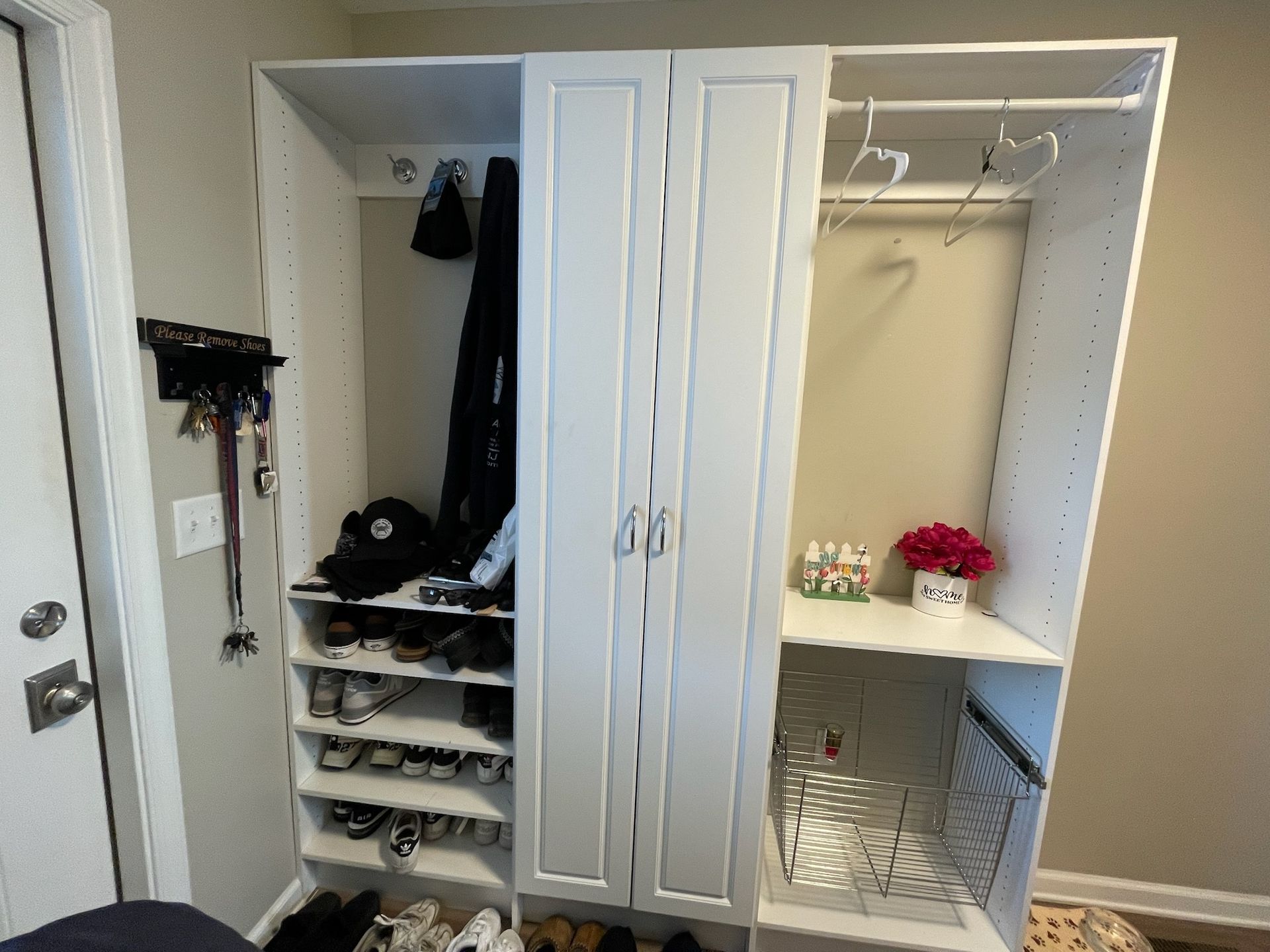A white, three-section storage unit with open shelves for shoes, a central cabinet, and a hanging area with a shelf.