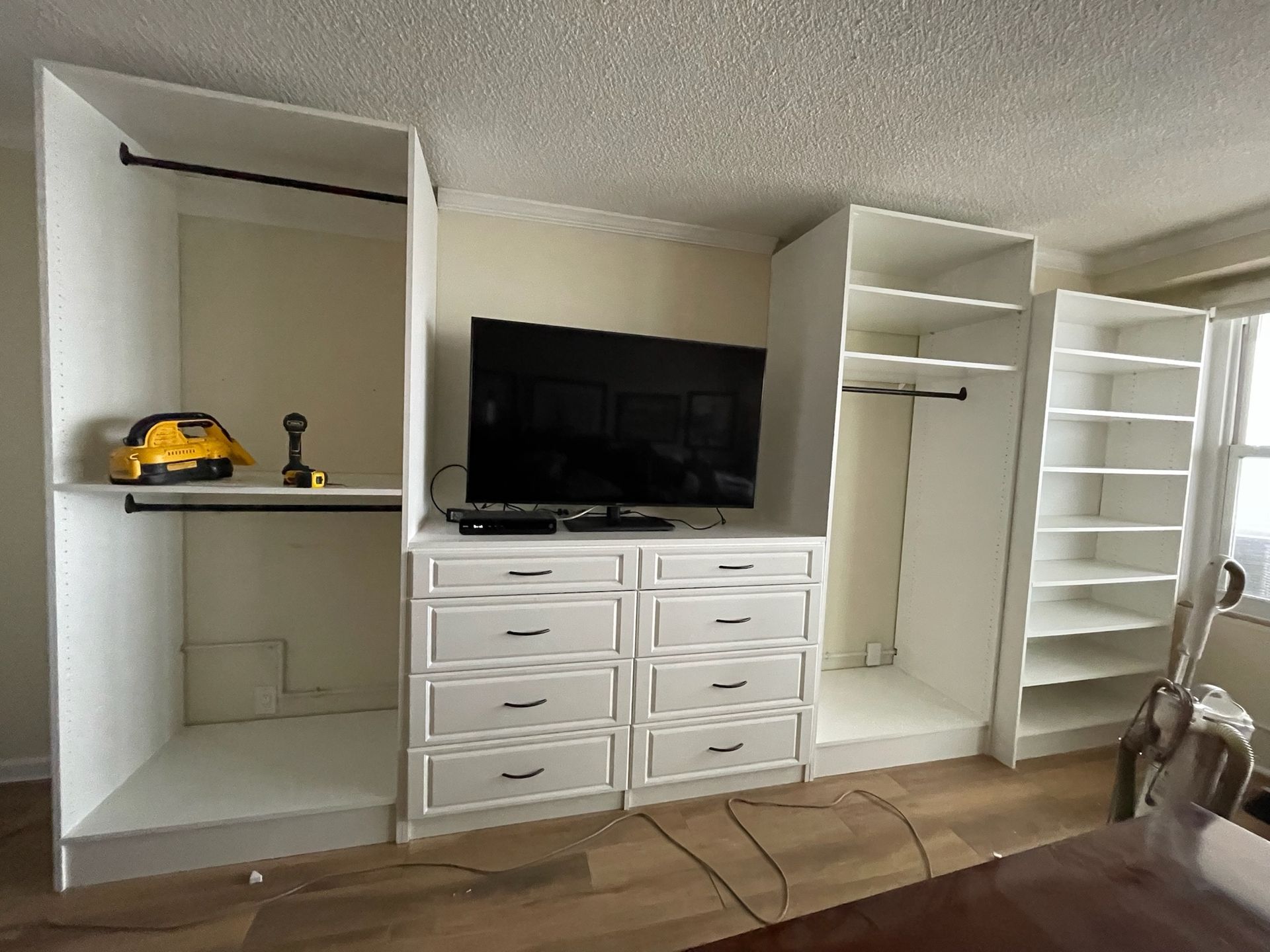 Custom white cabinetry installation with open closets, a central dresser with a TV on top, and a side shelving unit.