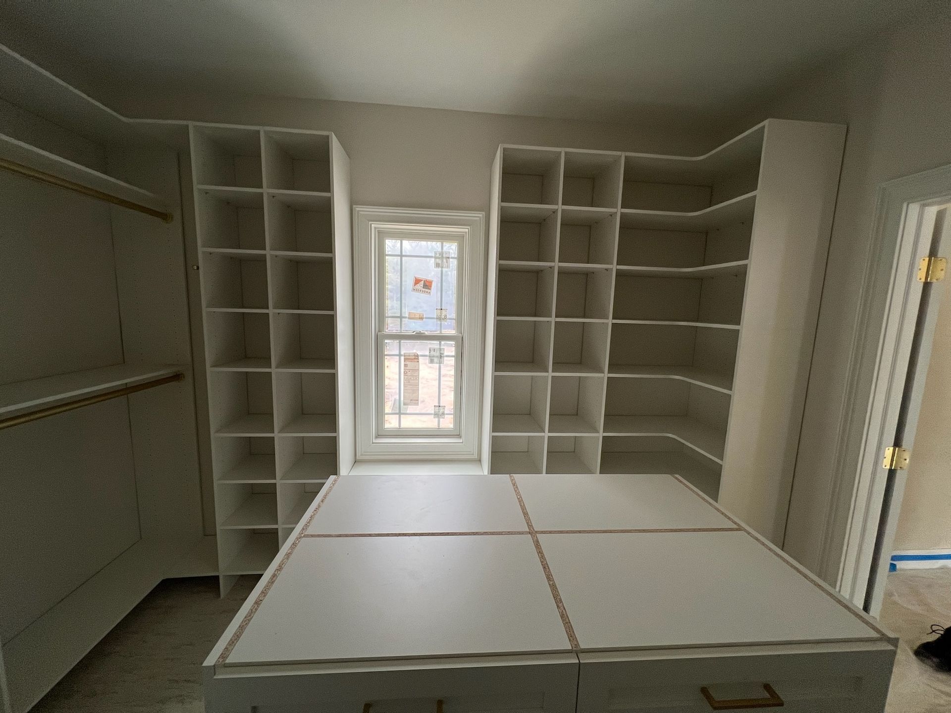 A walk-in closet featuring white built-in shelving, a large center island, and a centered window with natural light.