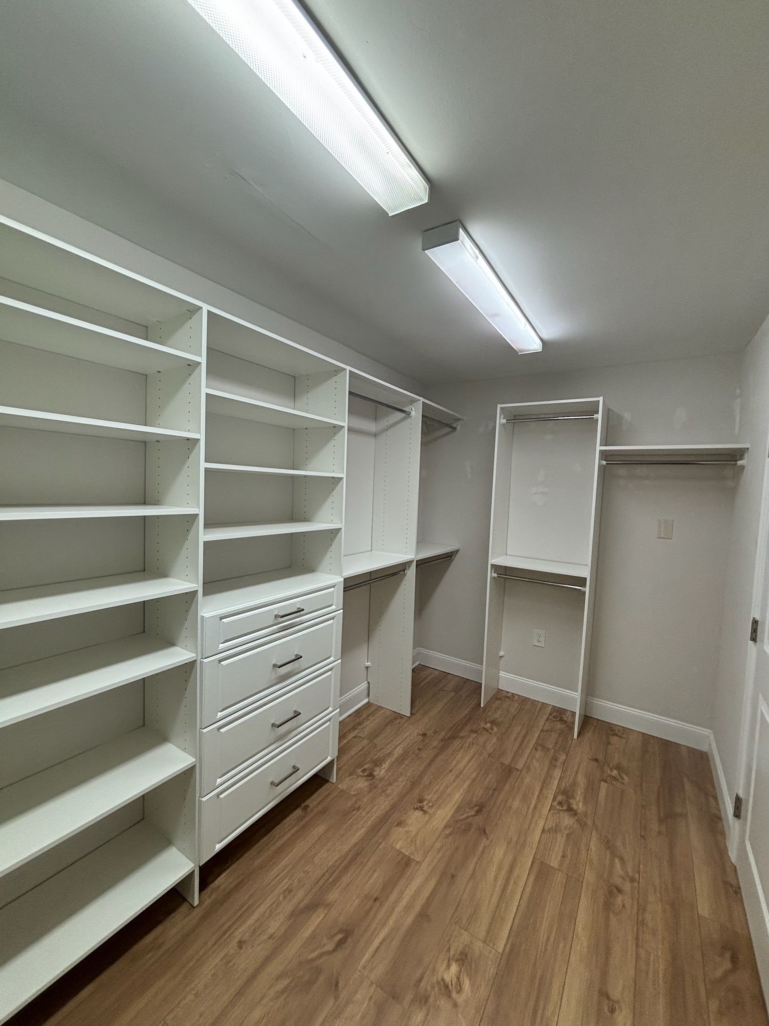 A bright walk-in closet with white shelving, a chest of drawers, hanging rods, and light wood flooring.