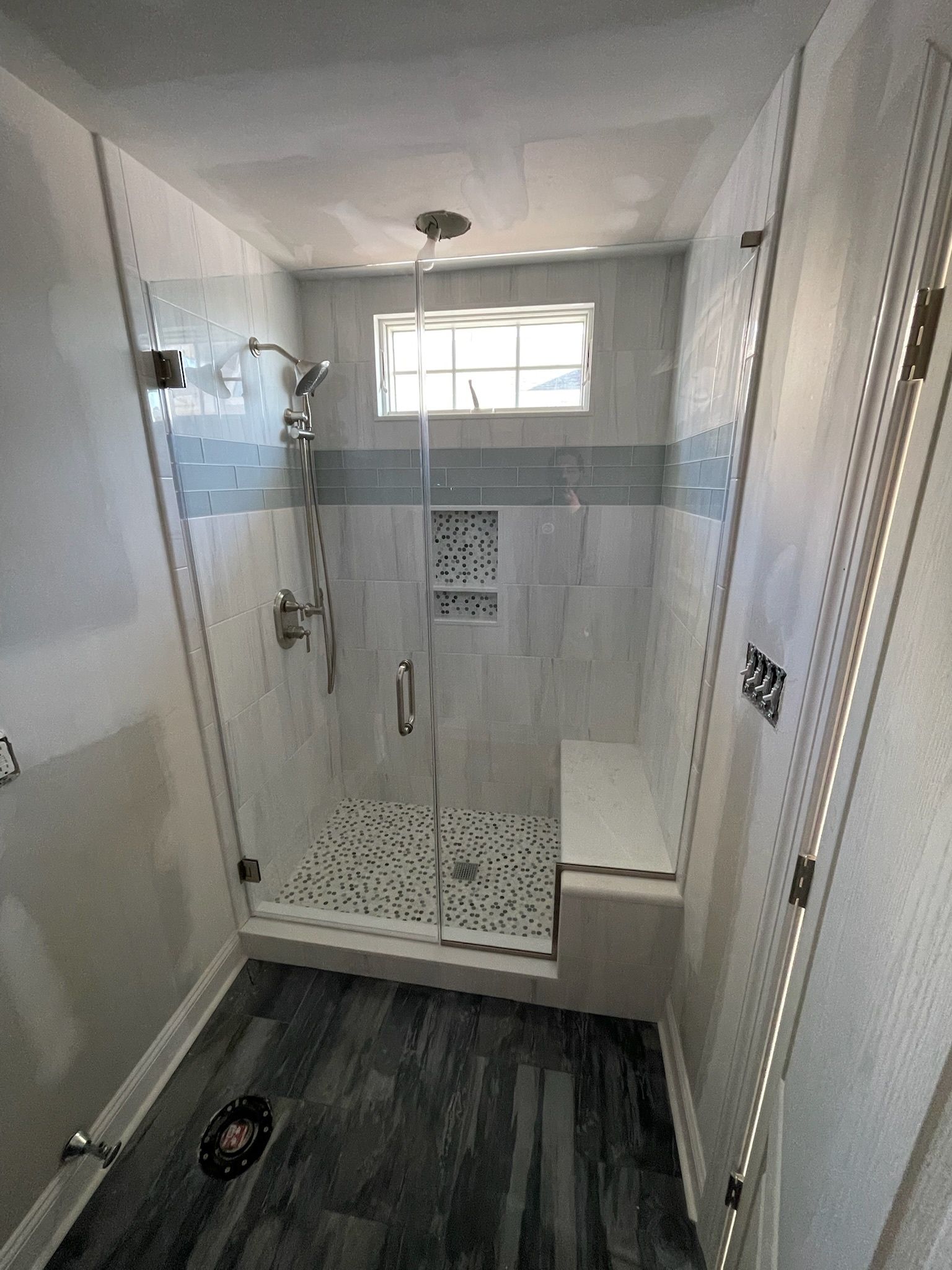 A modern walk-in shower with white tile walls, a patterned tile floor, a built-in bench, and a glass door.