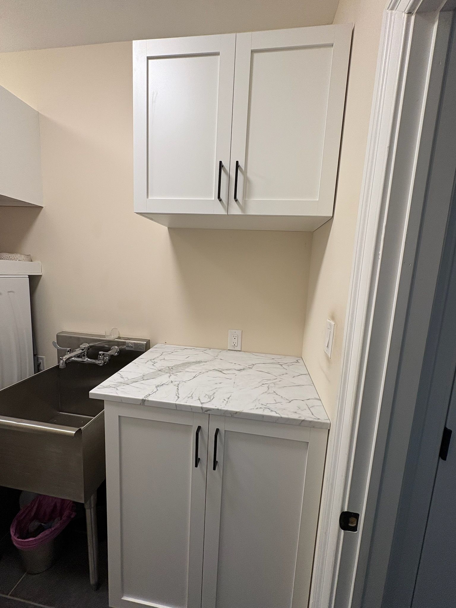 White cabinets with black handles, a marble-patterned countertop, and a utility sink in a laundry room.