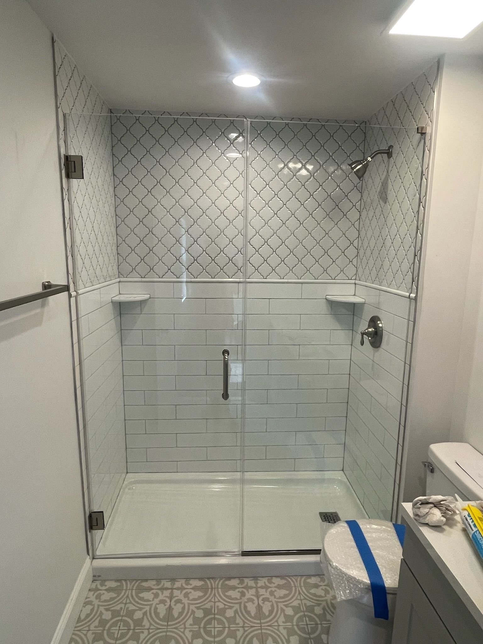 A modern bathroom featuring a glass-enclosed shower with white subway and geometric pattern tiles and chrome fixtures.
