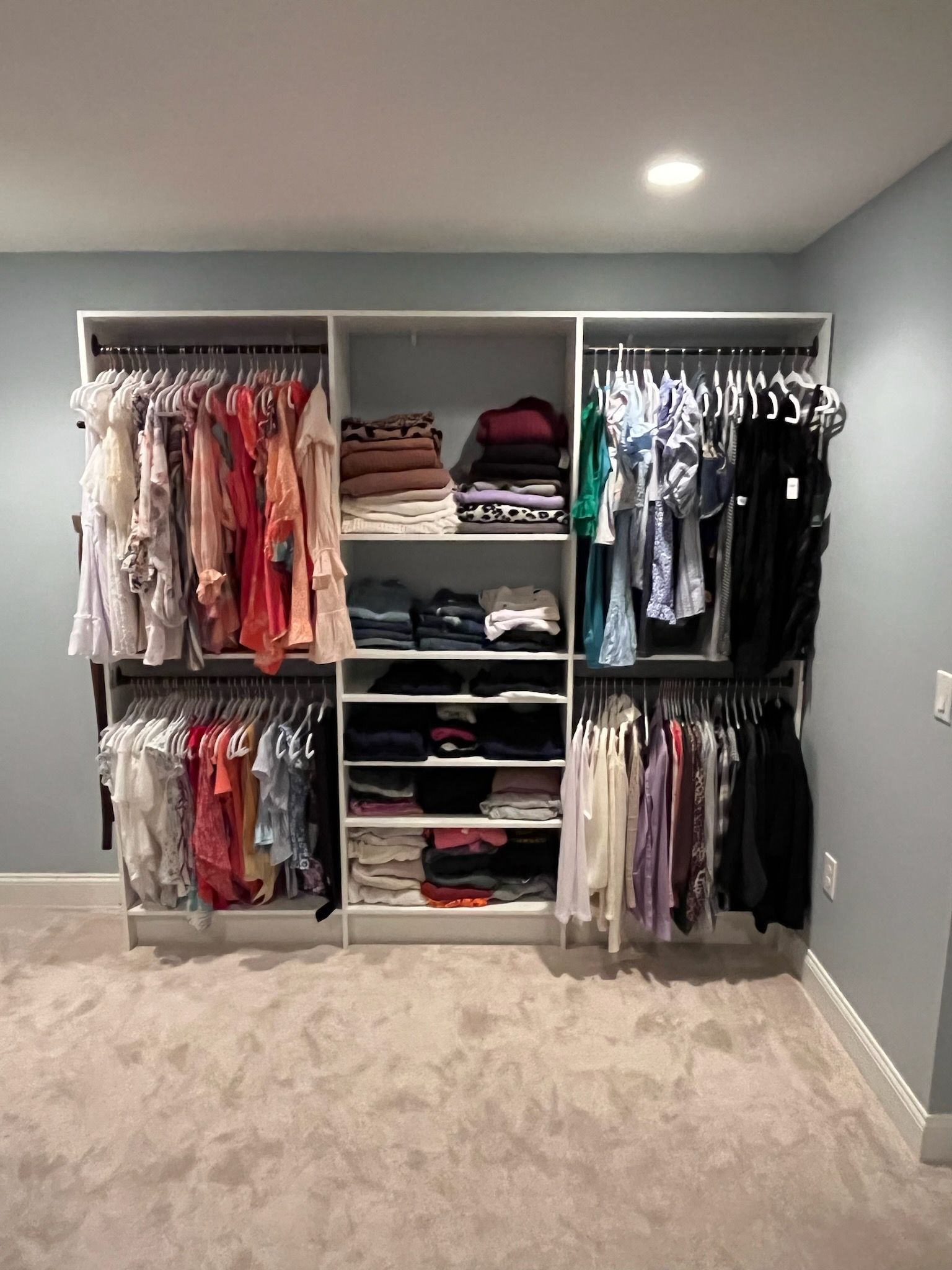A large, built-in white closet organizer against a light blue wall, featuring hanging clothes and folded shelf items.