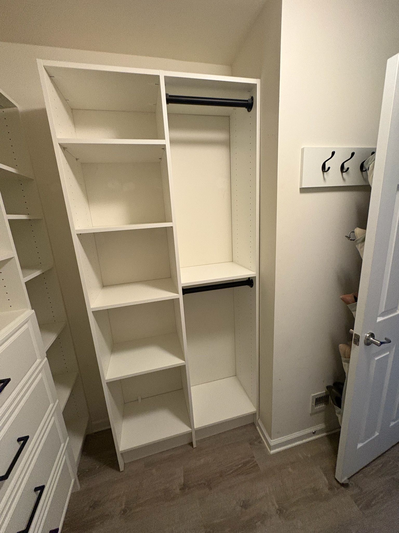 A white, custom-built closet organizer featuring shelves, a hanging rod, and a set of wall-mounted hooks nearby.
