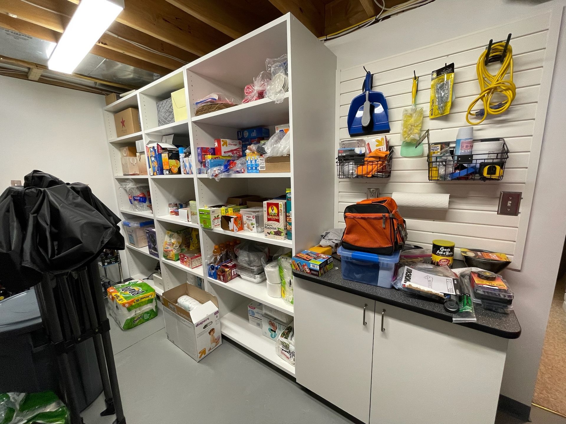 A storage room features white shelving units filled with various supplies, alongside a wall-mounted organizer.