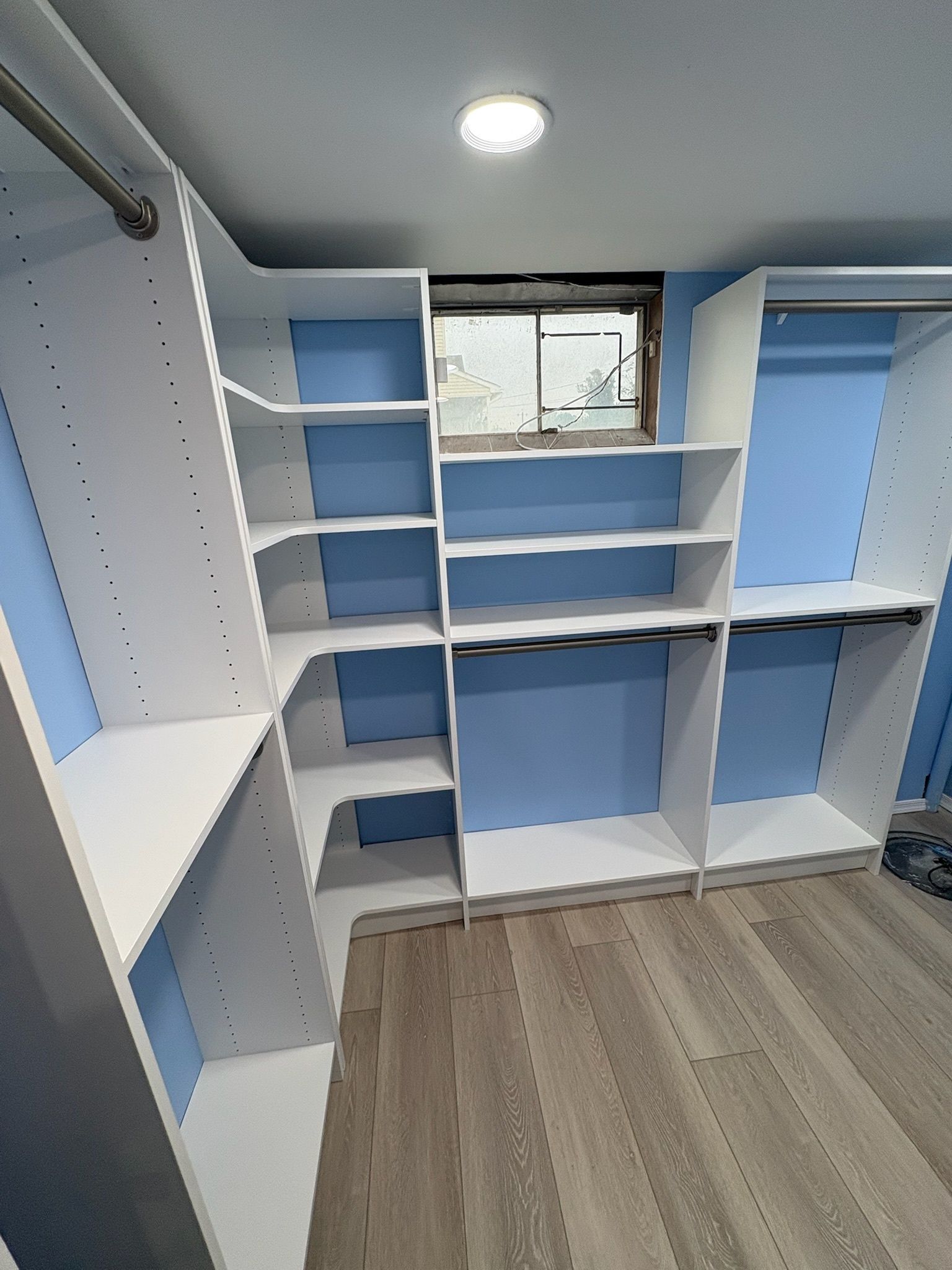 White custom closet shelving units with blue backing walls installed in a room with light wood-look flooring.