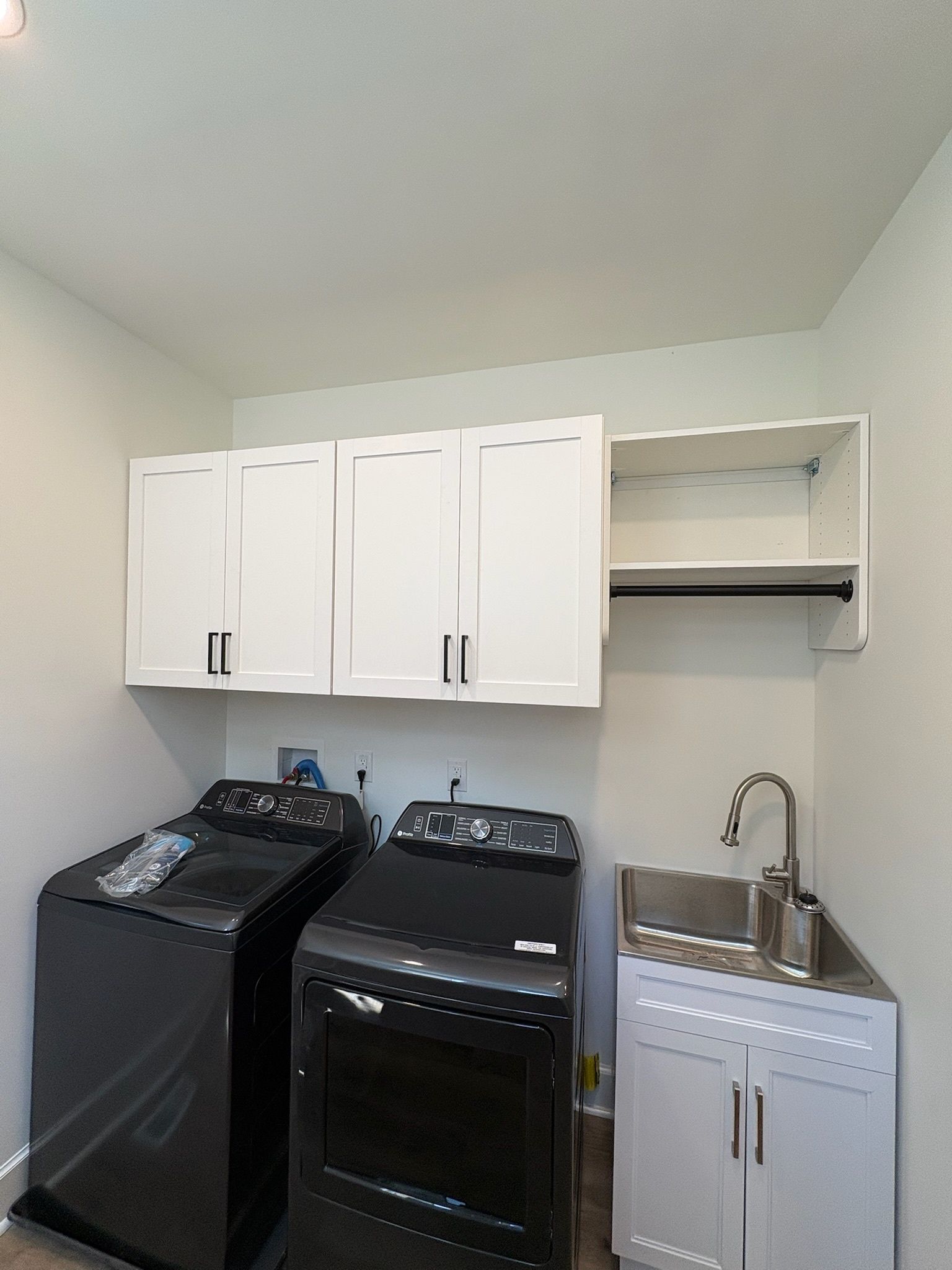 A laundry room with two black washing machines under white cabinets and a small utility sink with a faucet.