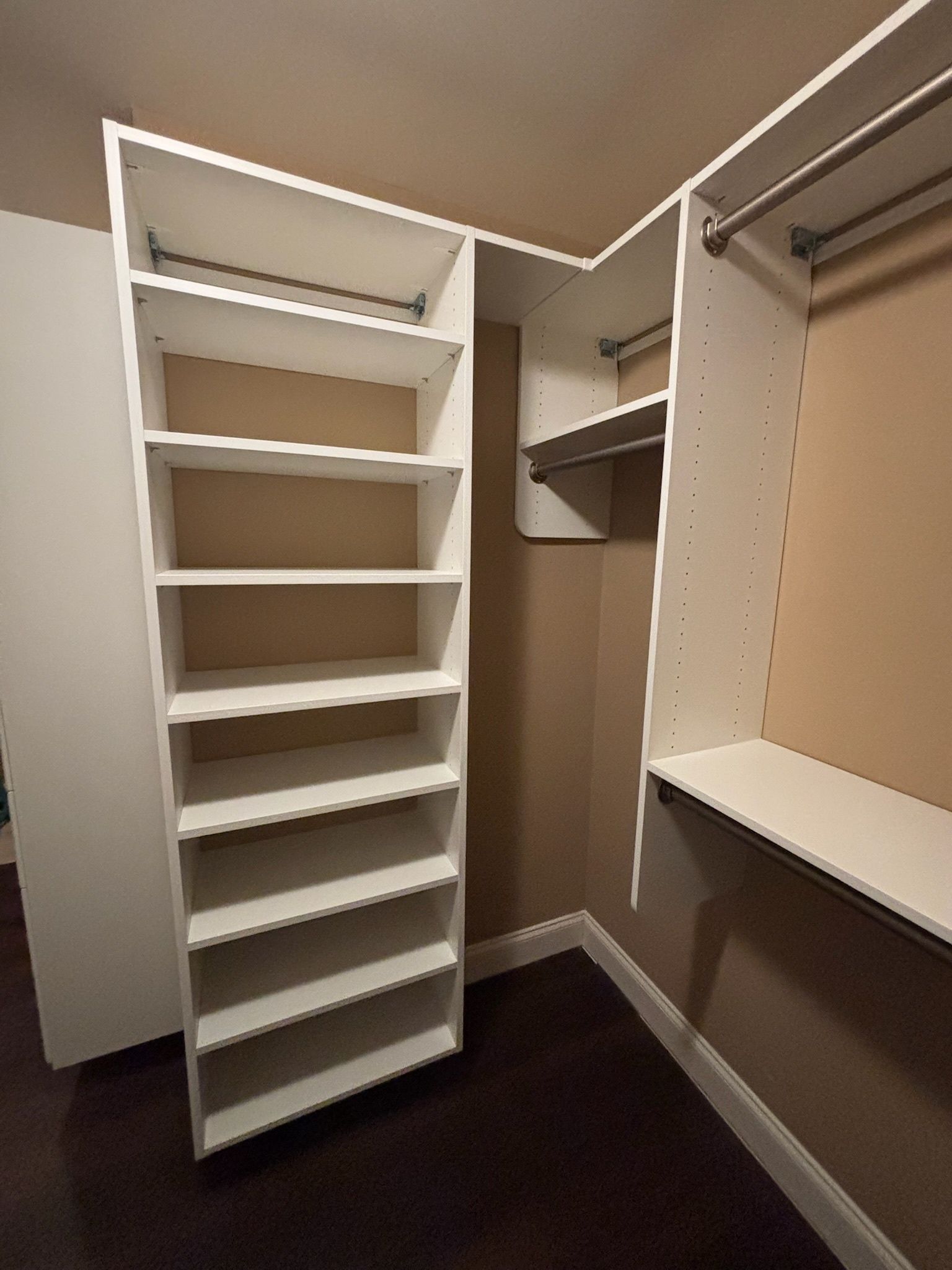 A white, L-shaped closet organizer with shelves on the left and a hanging rod on the right inside a walk-in closet.