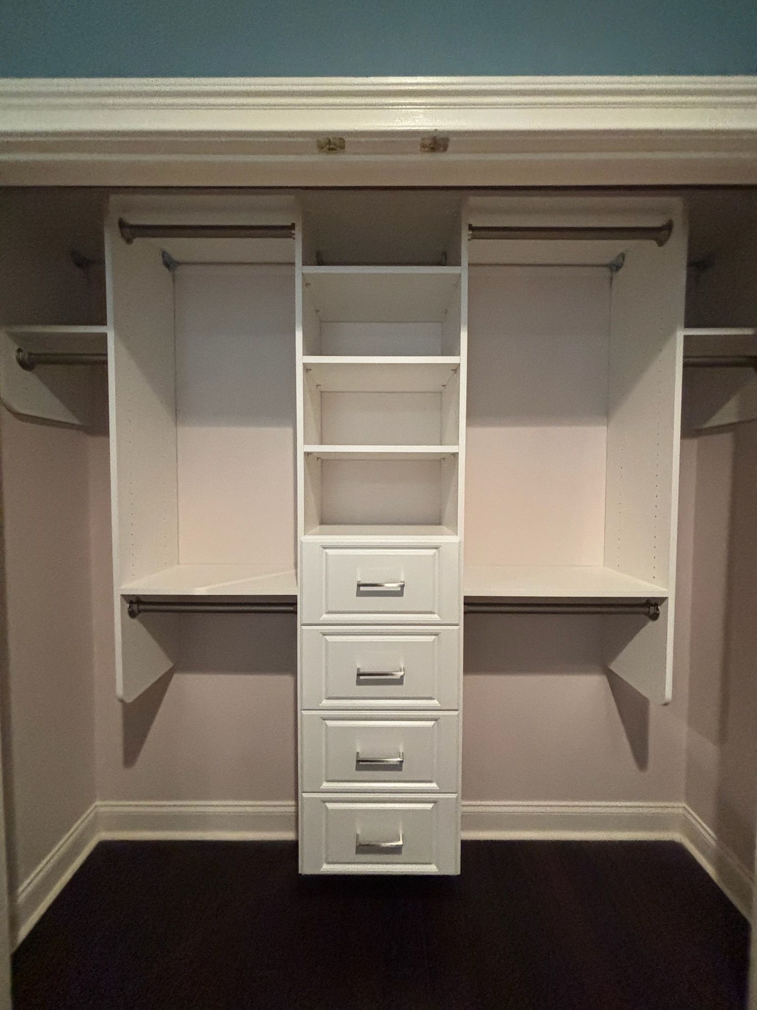 A white closet organizer with a central tower of four drawers and three open shelves, flanked by two clothing rods.