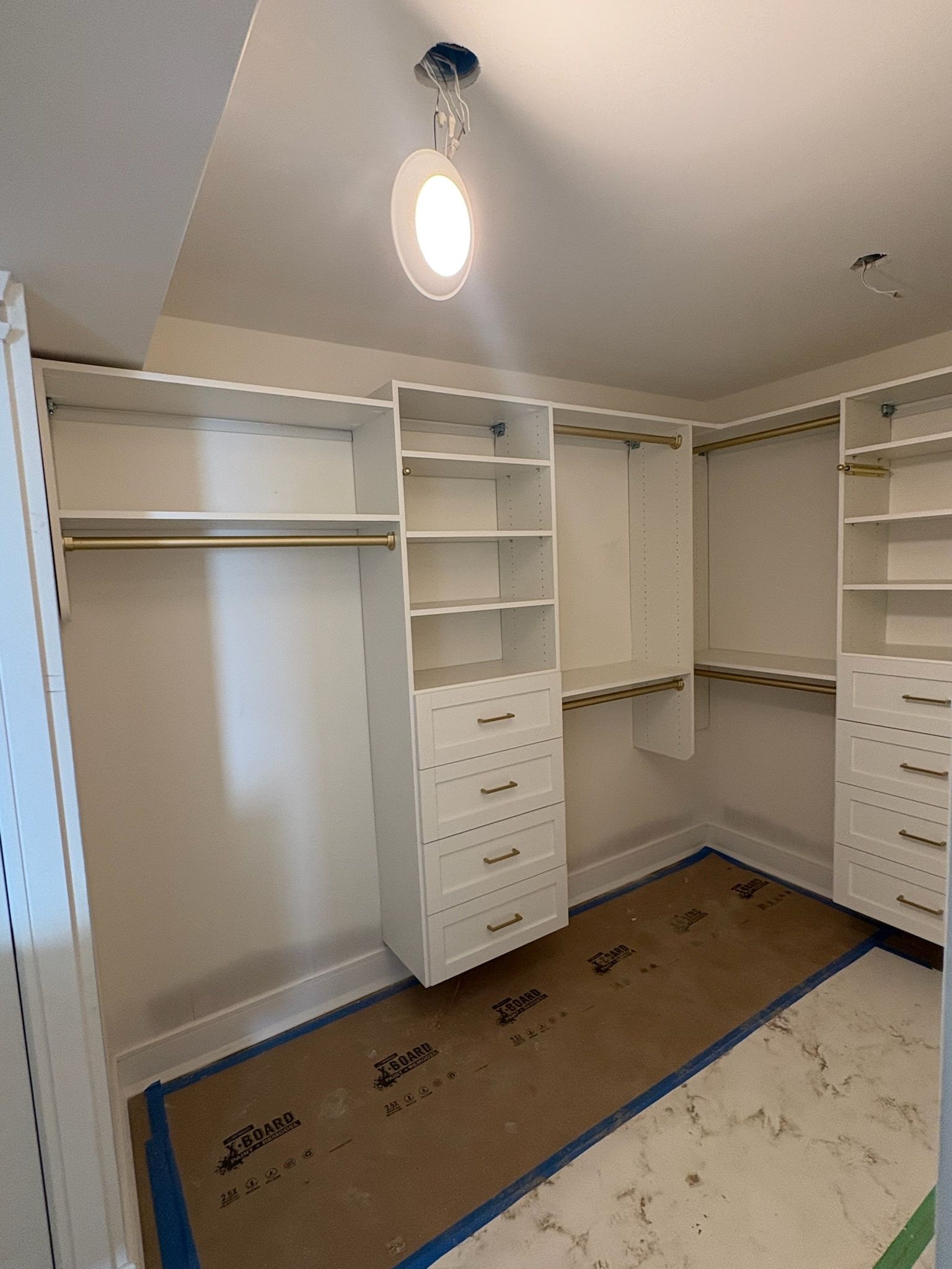 A walk-in closet featuring white built-in shelving, drawers, and hanging rods with gold hardware on a partially tiled floor.