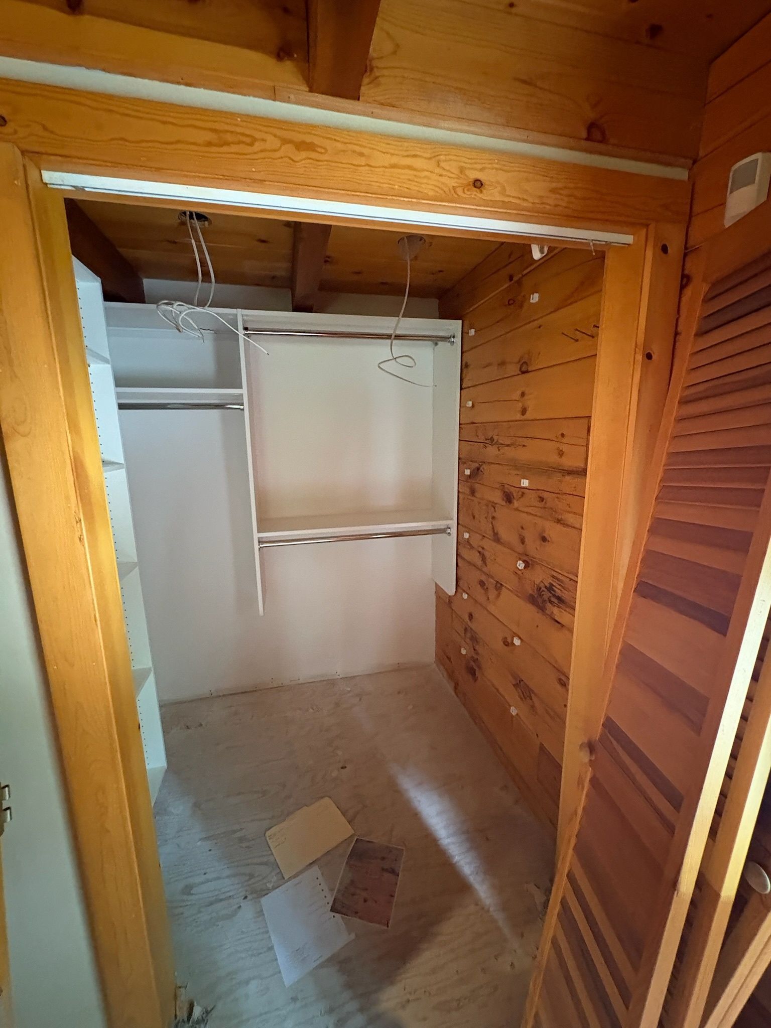 A walk-in closet under construction with white shelving units mounted against rustic wood-paneled walls.