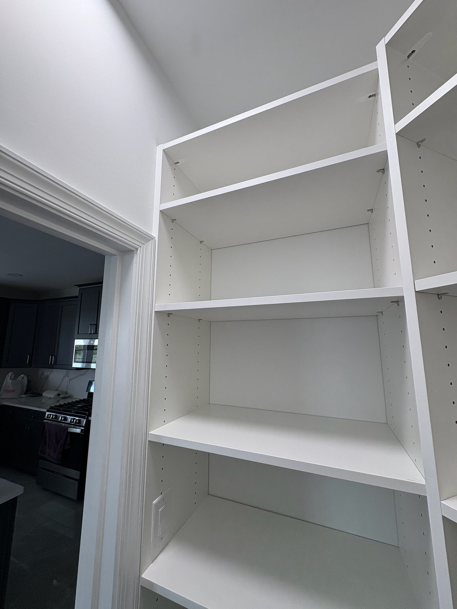 A low-angle view of white, empty adjustable shelving units positioned beside a doorway.