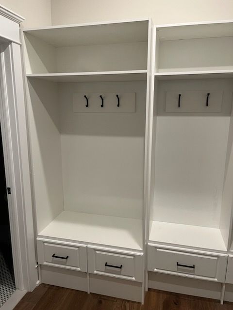 A white built-in mudroom locker unit with upper shelves, rows of black coat hooks, and lower storage drawers.