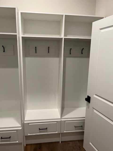 White wooden mudroom storage units with built-in shelves, coat hooks, and drawers, partially obscured by a white door.
