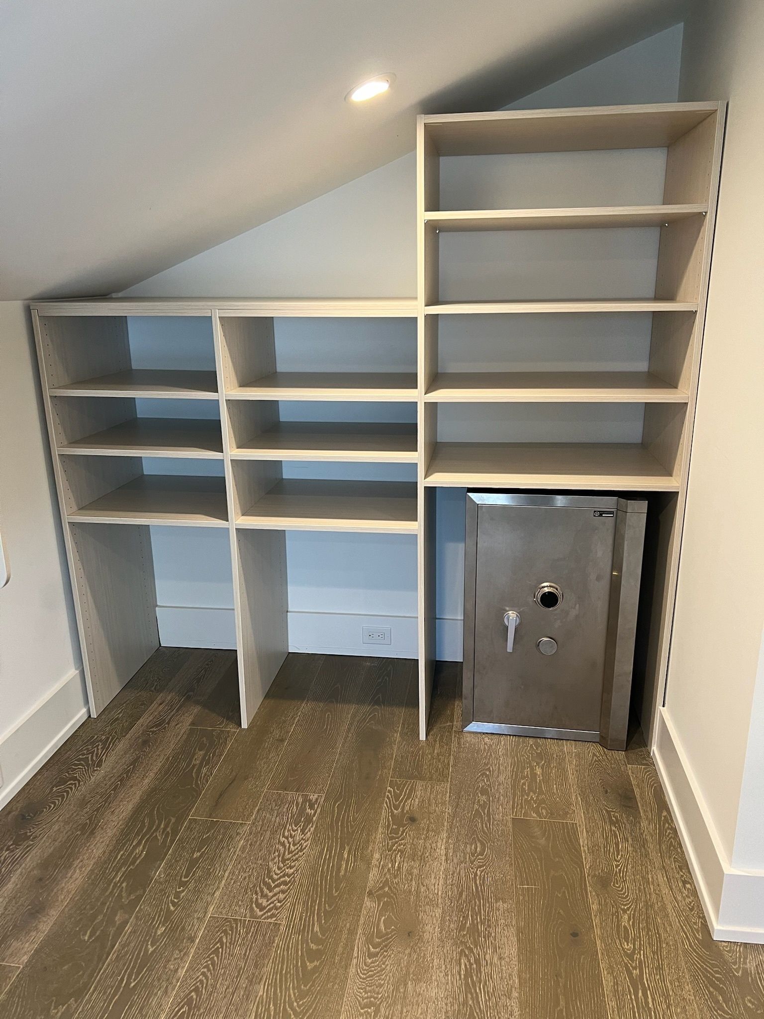 Custom shelving unit in an attic with slanted ceilings, featuring various storage cubbies and a metal floor safe.