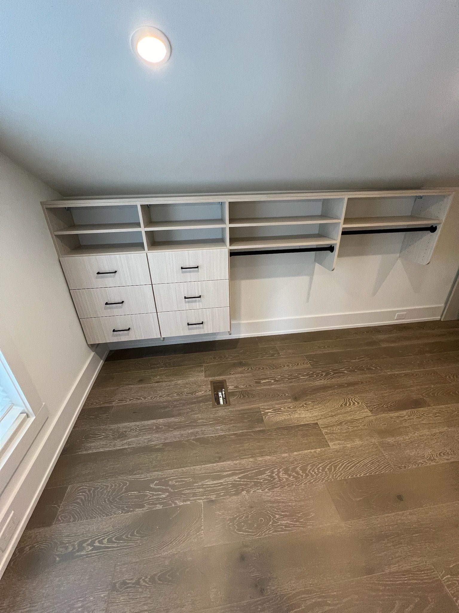 A walk-in closet featuring light wood built-in shelving, drawers, and hanging rods under a sloped ceiling.