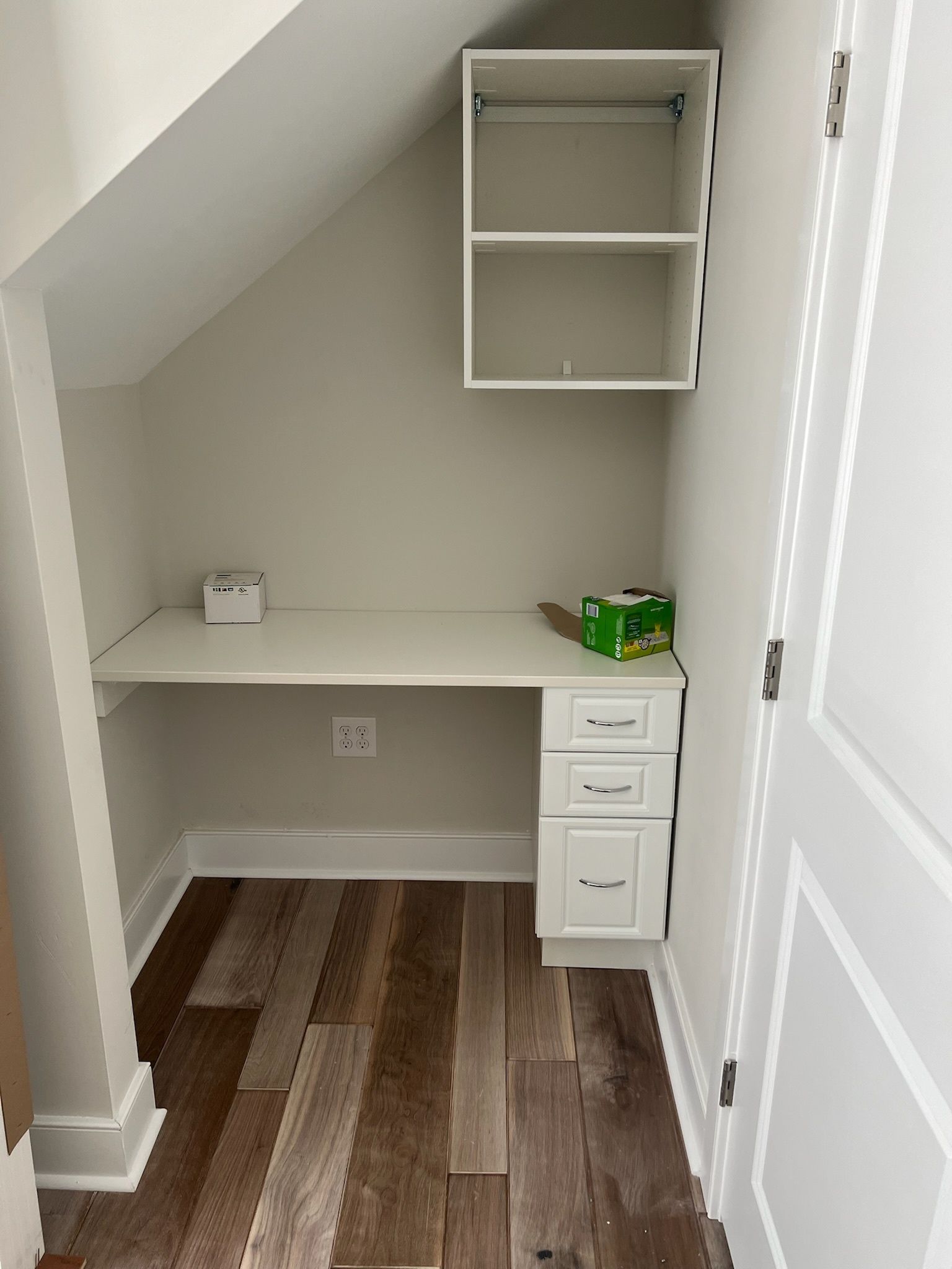 A small nook features a built-in white desk with drawers, a matching overhead shelf, and brown wood-look flooring.