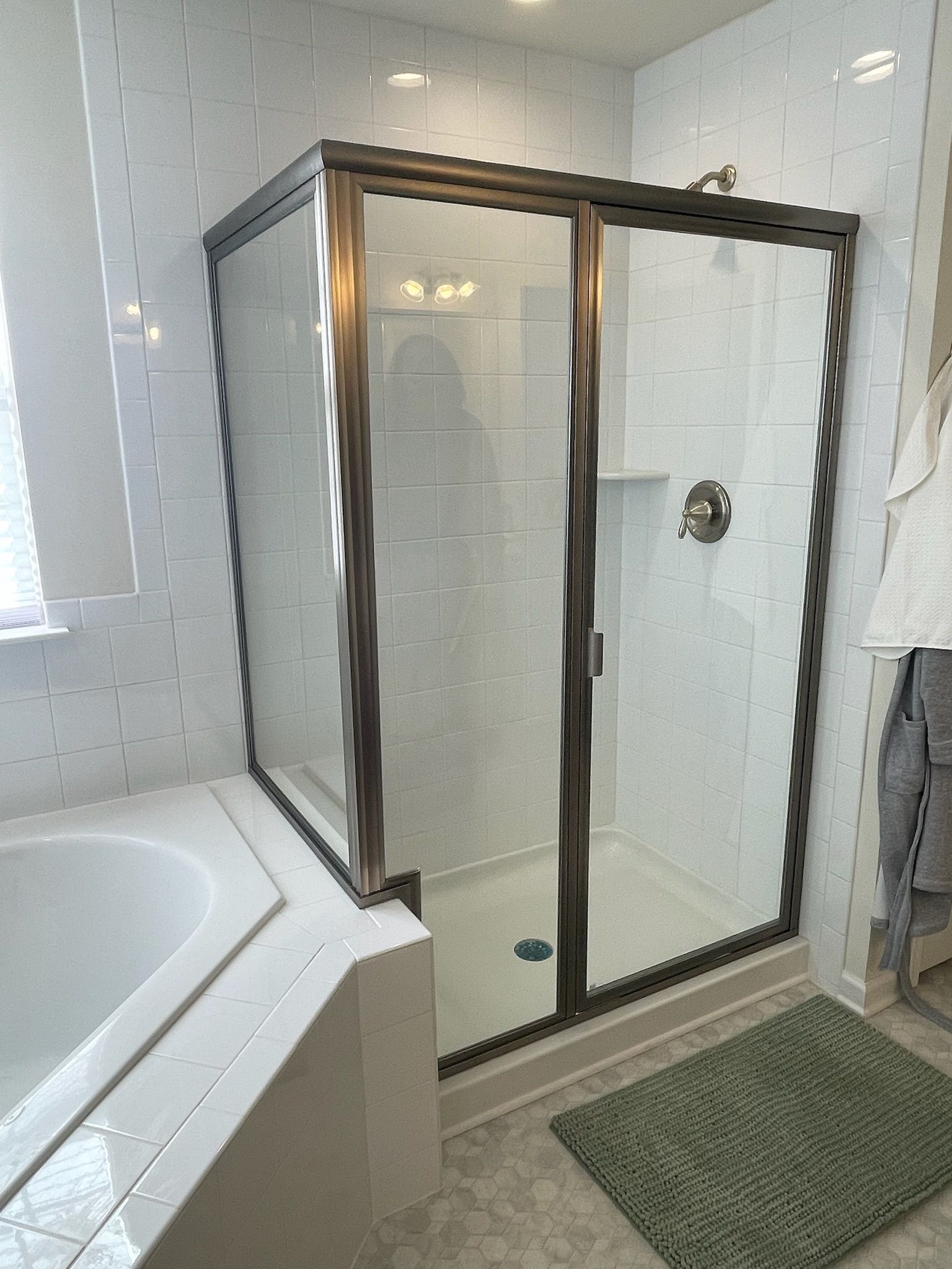 A walk-in shower with a bronze frame and glass door located next to a white bathtub in a tiled bathroom.
