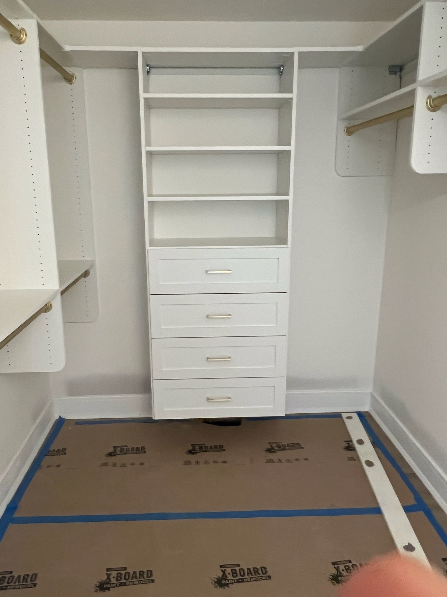 A white closet organizer with shelving and four drawers installed in a room under construction with floor protection.