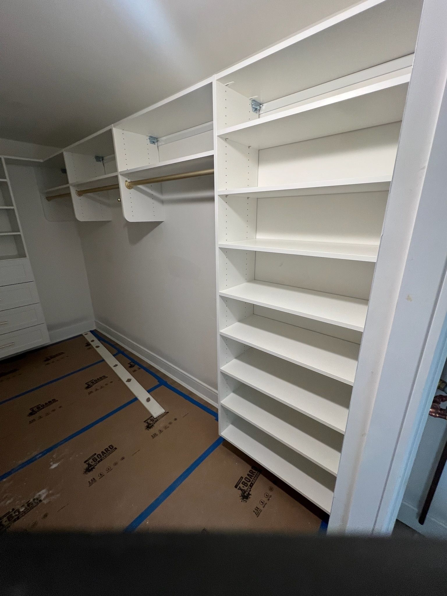 White closet storage unit featuring shelves and hanging rods, with construction paper covering the floor.