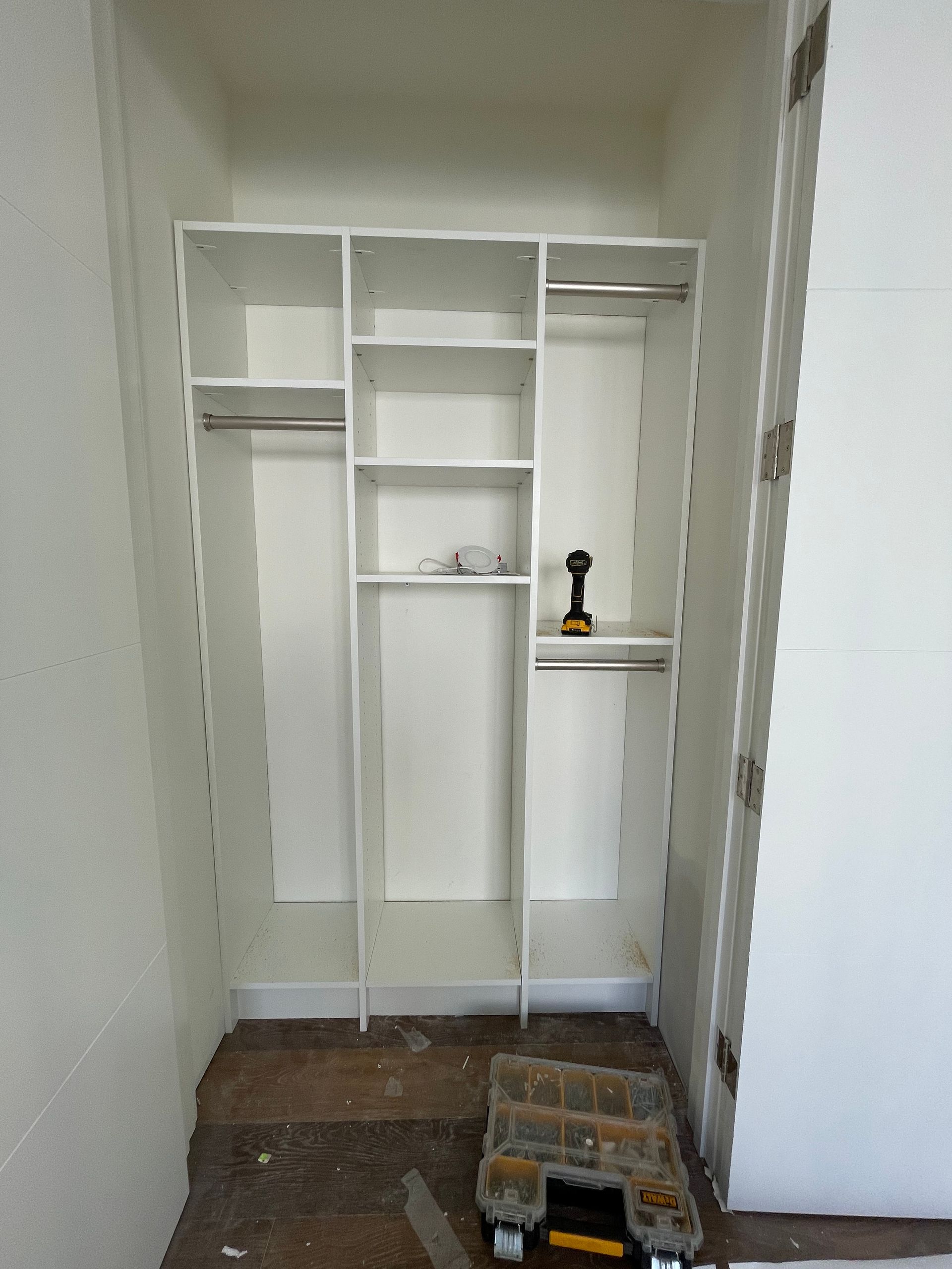 A newly installed white closet organizer with shelves and hanging rods, viewed inside an unfinished room.