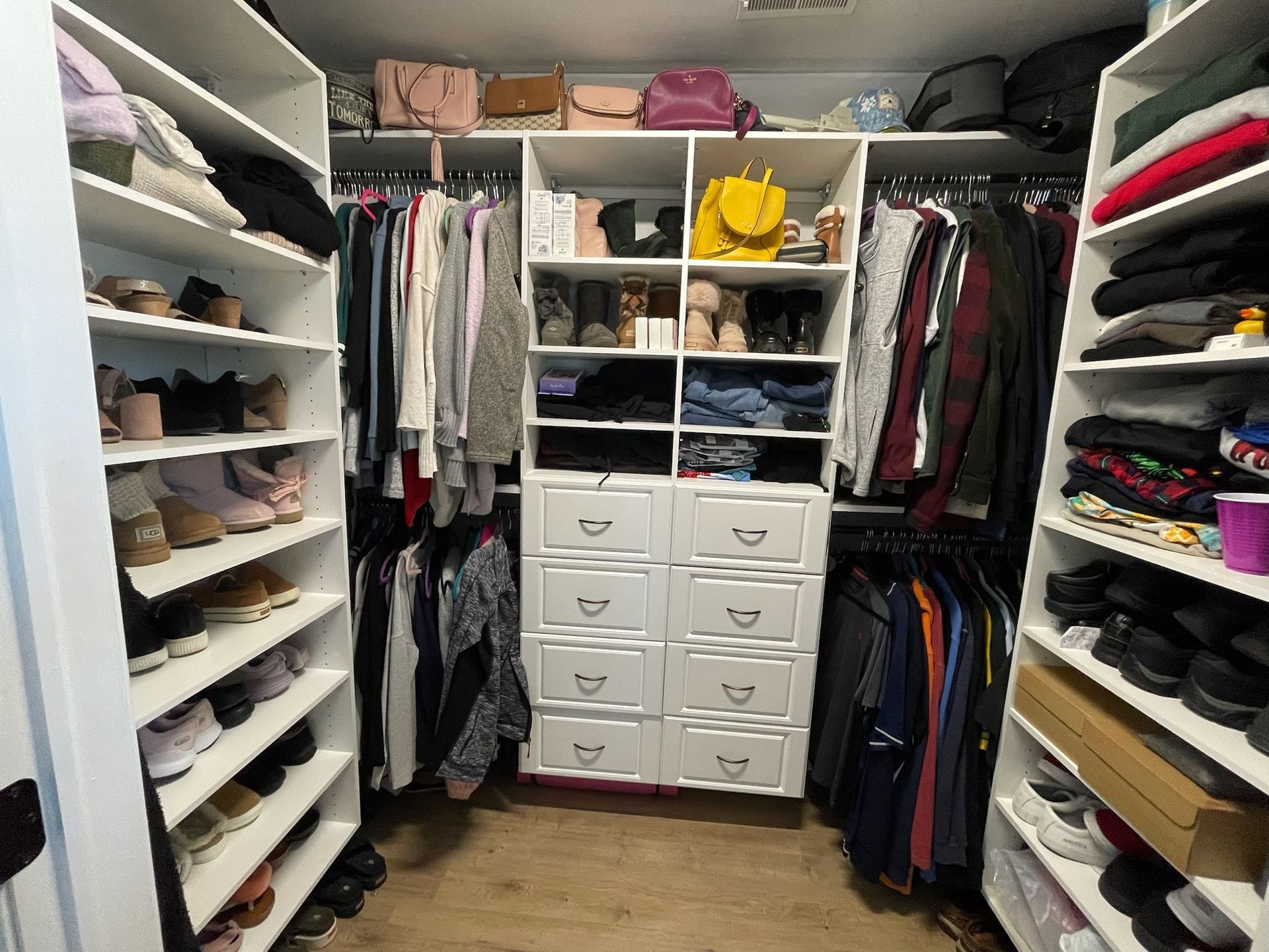 A well-organized walk-in closet featuring shelves with shoes, clothing racks, and white drawers.