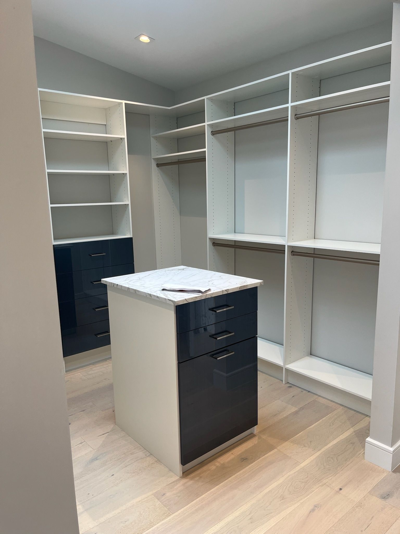 A walk-in closet featuring white shelves, hanging rods, and dark blue drawers with a matching central island.