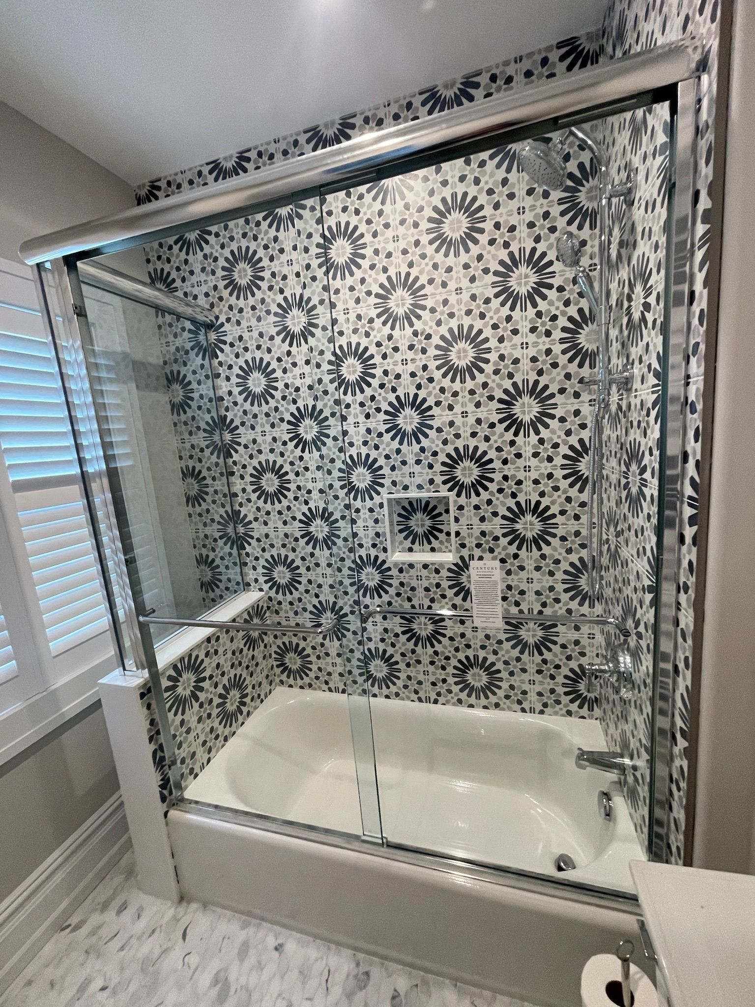 A bathtub with a sliding glass door and black and white patterned tile on the surrounding walls.
