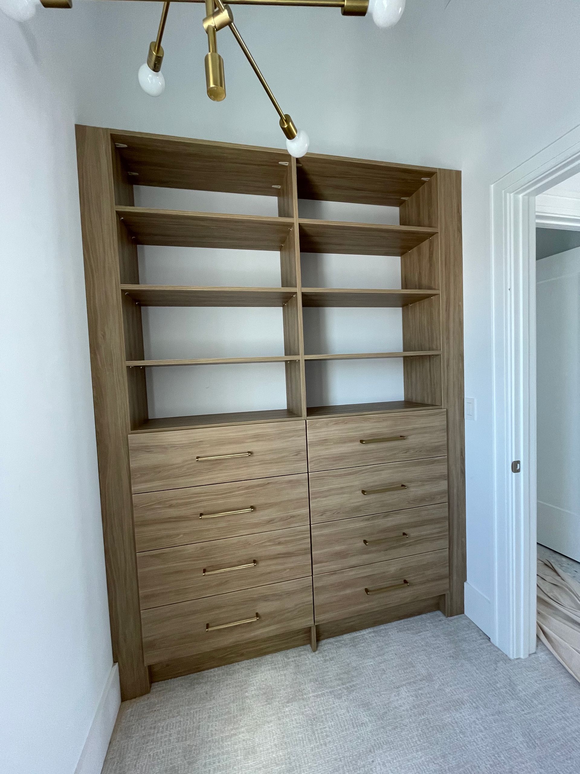 A floor-to-ceiling wooden shelving unit with open shelves on top and eight drawers on the bottom in a room with carpet.