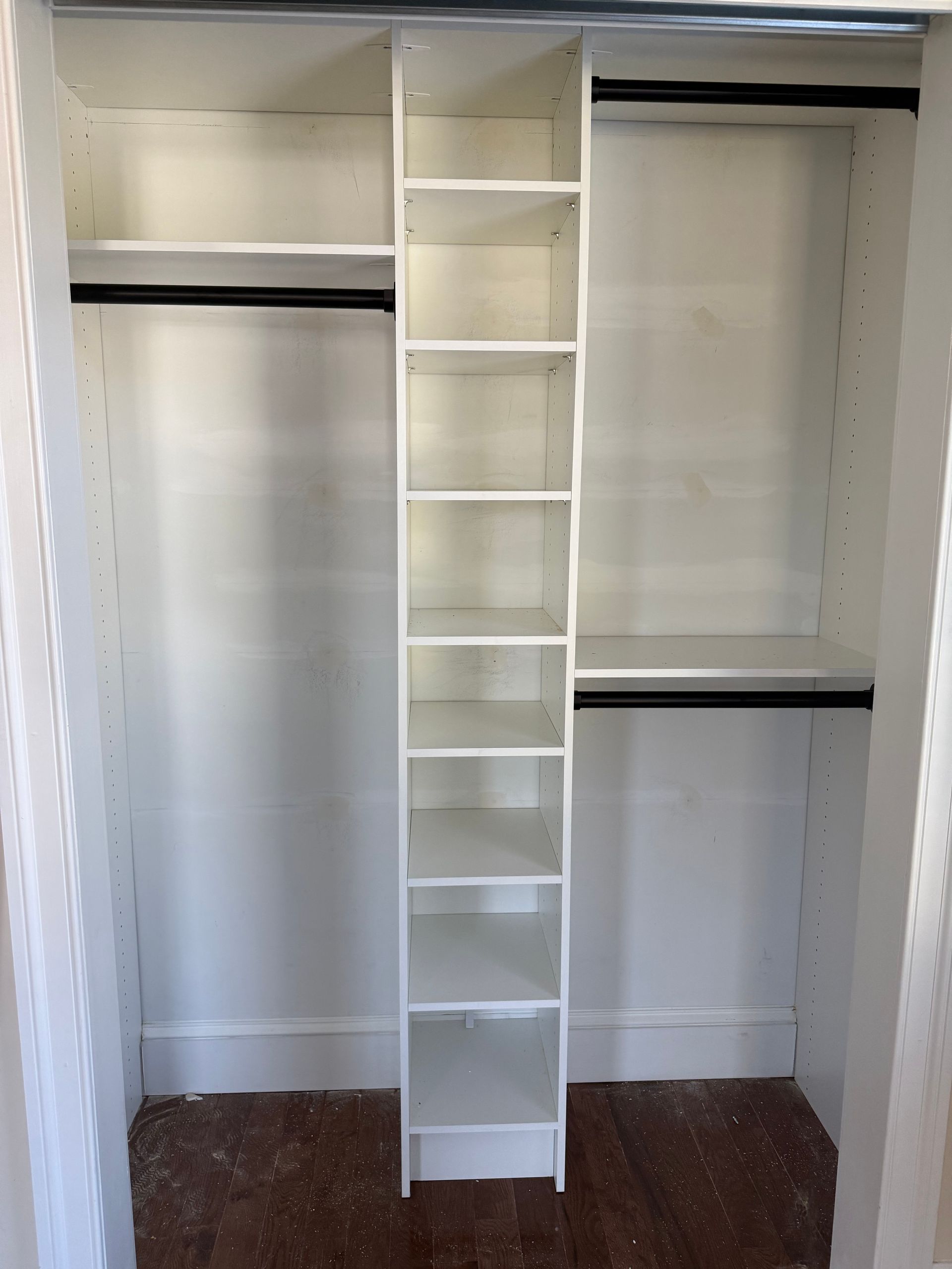 An empty white closet with a central vertical shelving unit and hanging rods on either side.