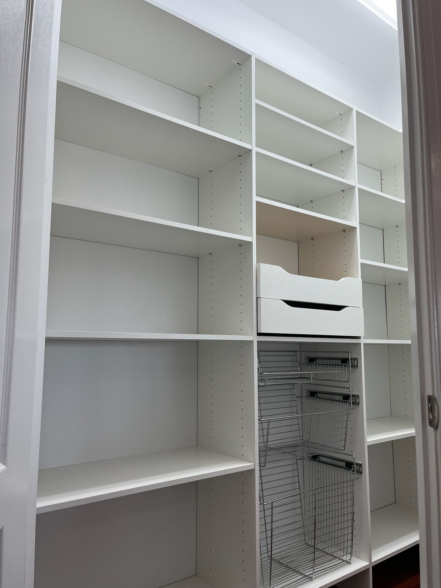 White built-in closet shelving unit featuring open shelves, two white drawers, and a lower metal pegboard section.