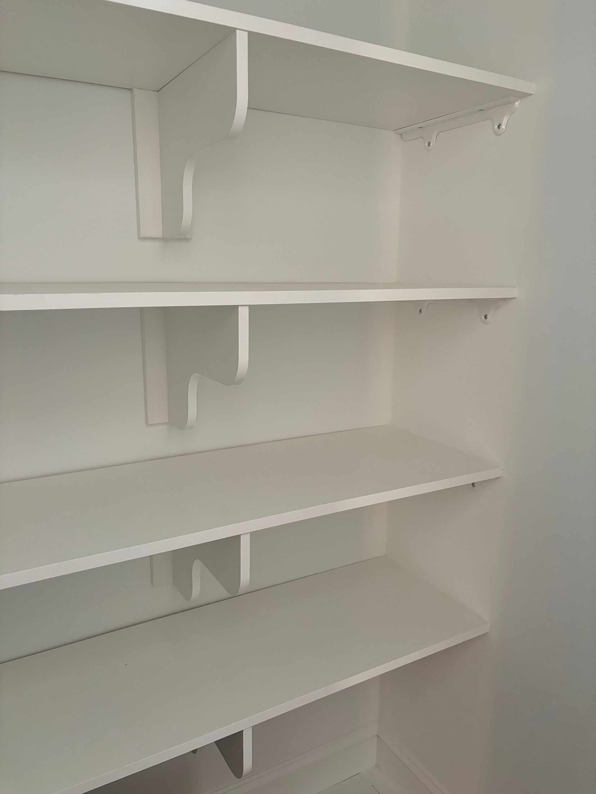 White shelving unit installed in a corner, featuring four wooden shelves supported by painted wall brackets.