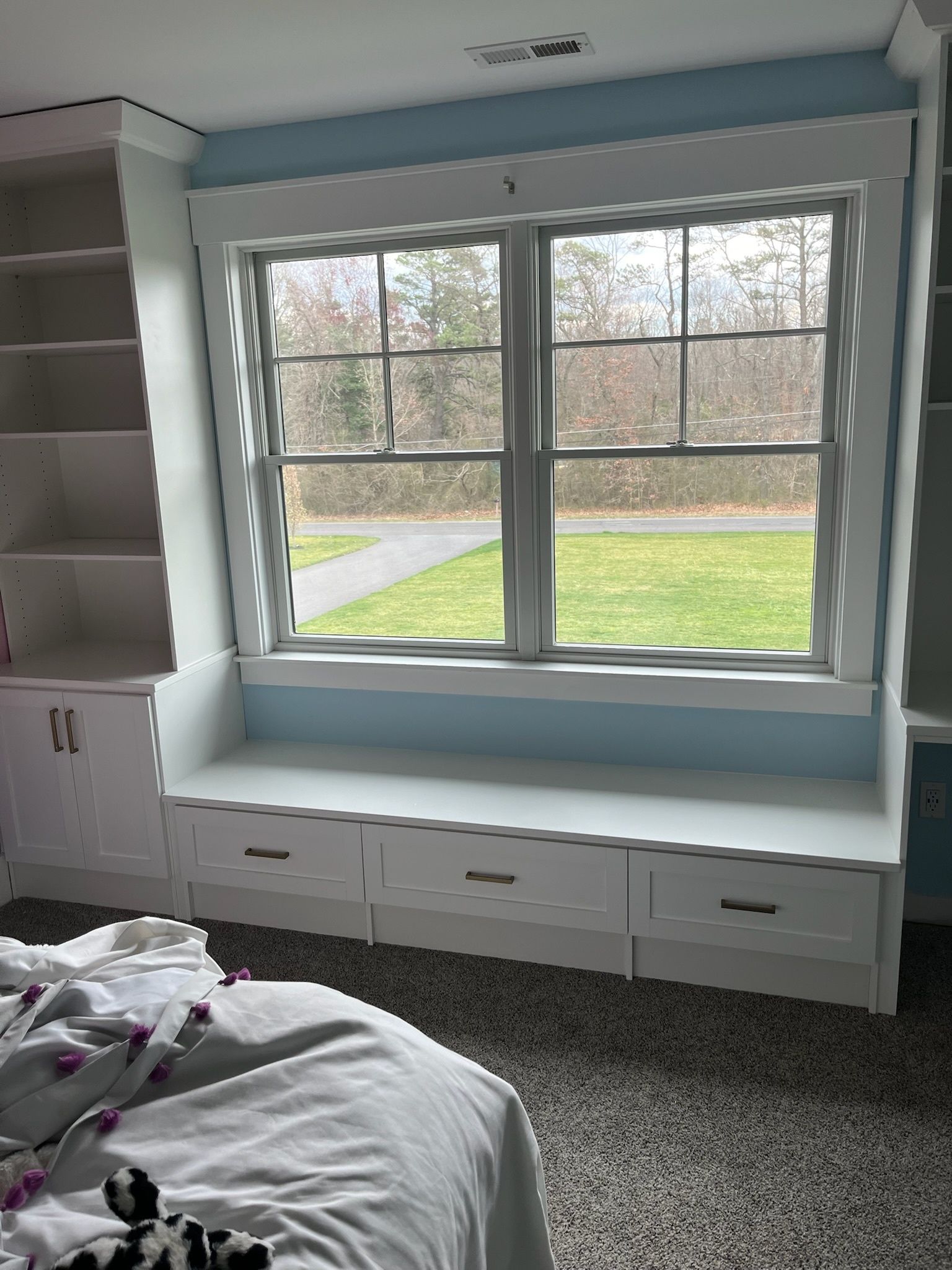 Built-in white bench seat with storage drawers below, positioned beneath a window with tall shelving on the sides.