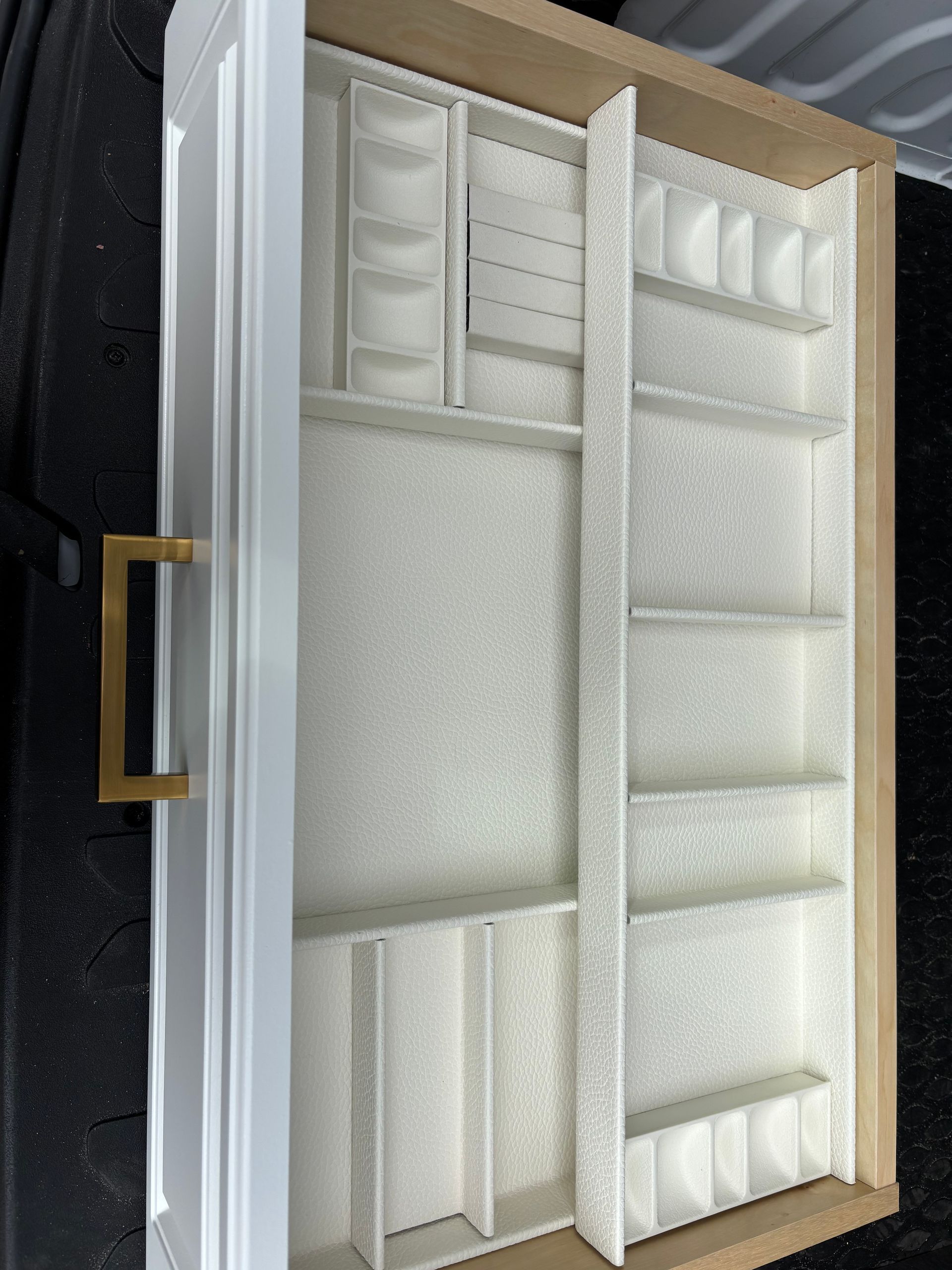 White, velvet-lined jewelry drawer organizer with multiple compartments and a gold handle, viewed from above.