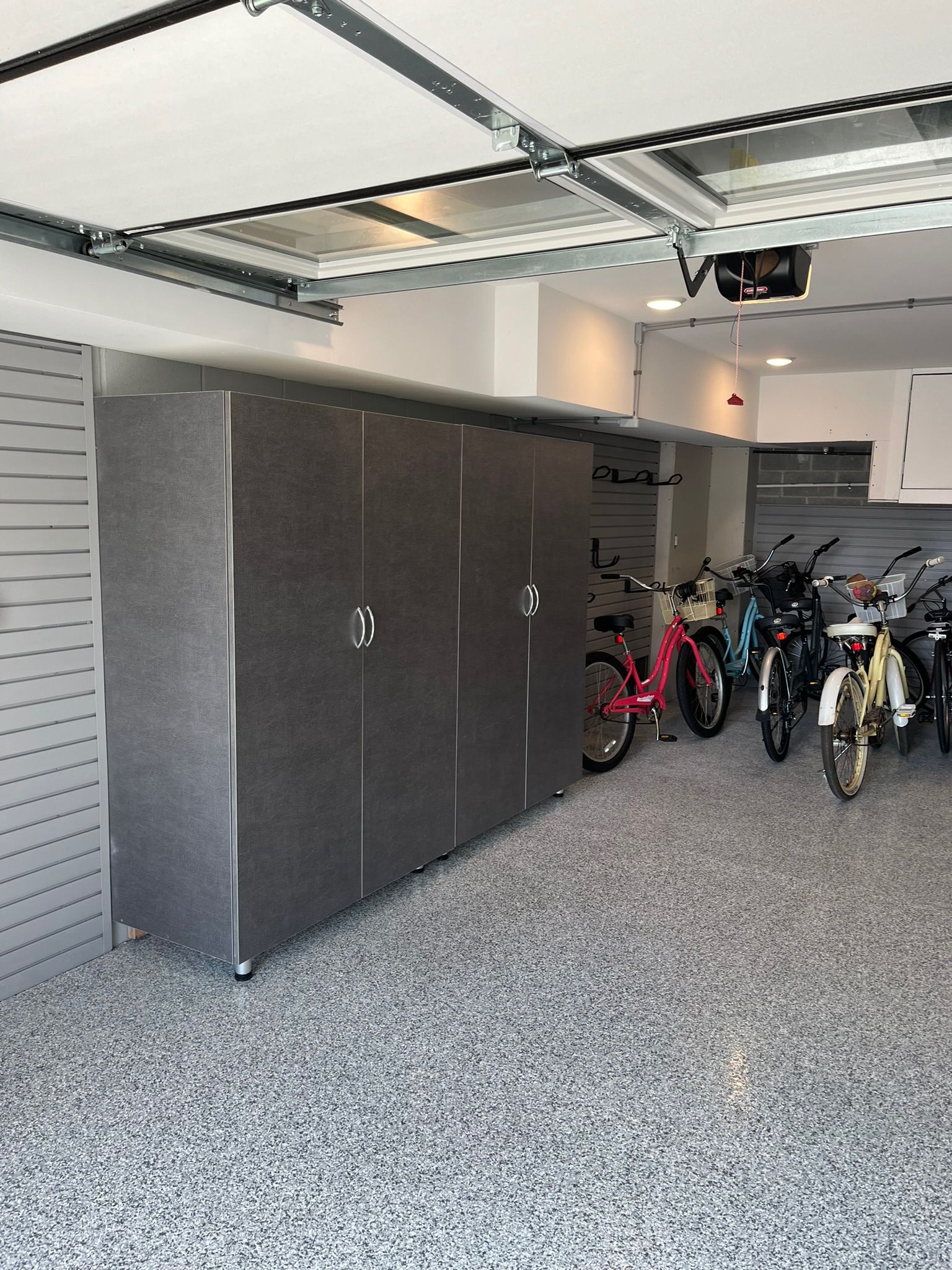 A garage with a large grey cabinet, grey speckled flooring, and several bicycles parked along the back wall.