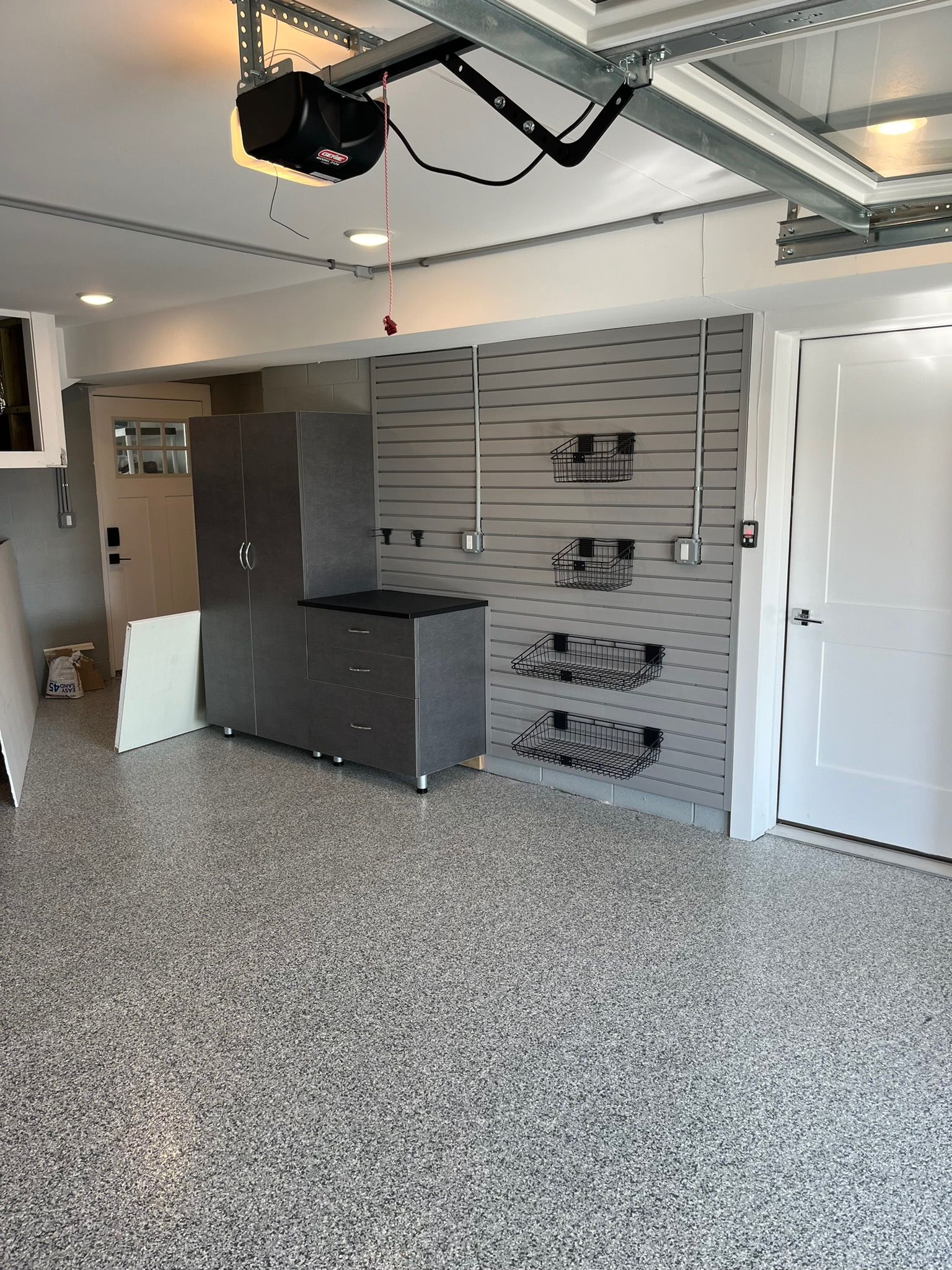 A modern garage with speckled flooring, a tall grey storage cabinet with counter, and grey wall-mounted storage panels.