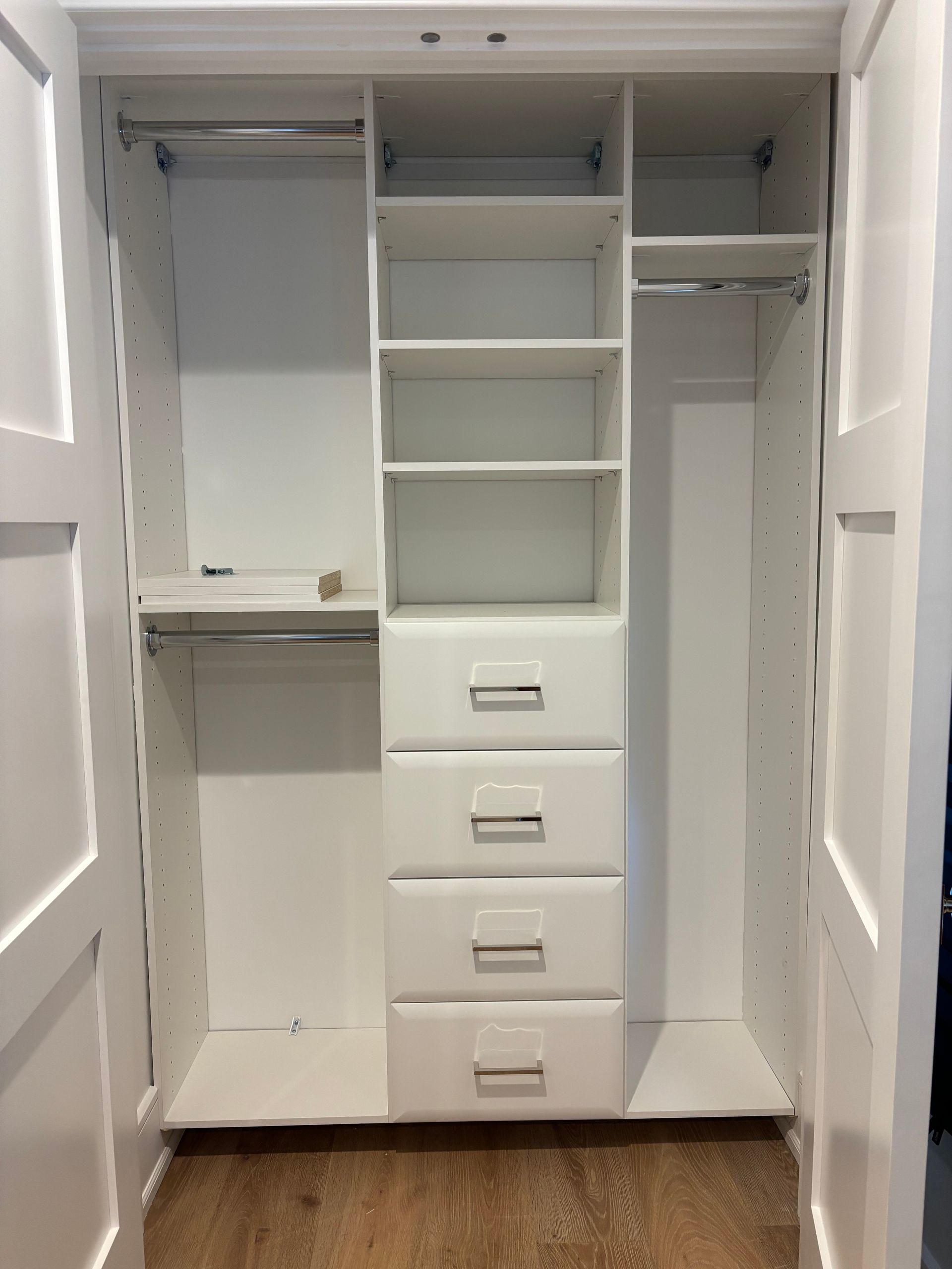 A white reach-in closet with shelves, four drawers, and hanging rods on the left and right sides.