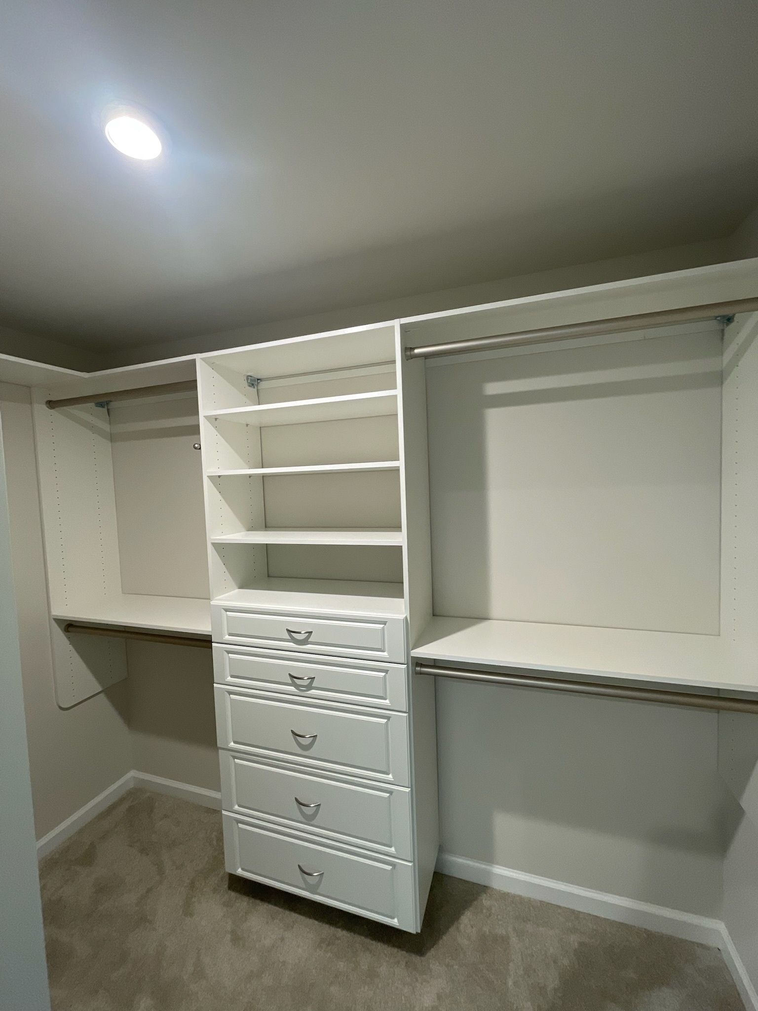 A white walk-in closet featuring a central drawer unit with open shelving above and hanging rods on both sides.